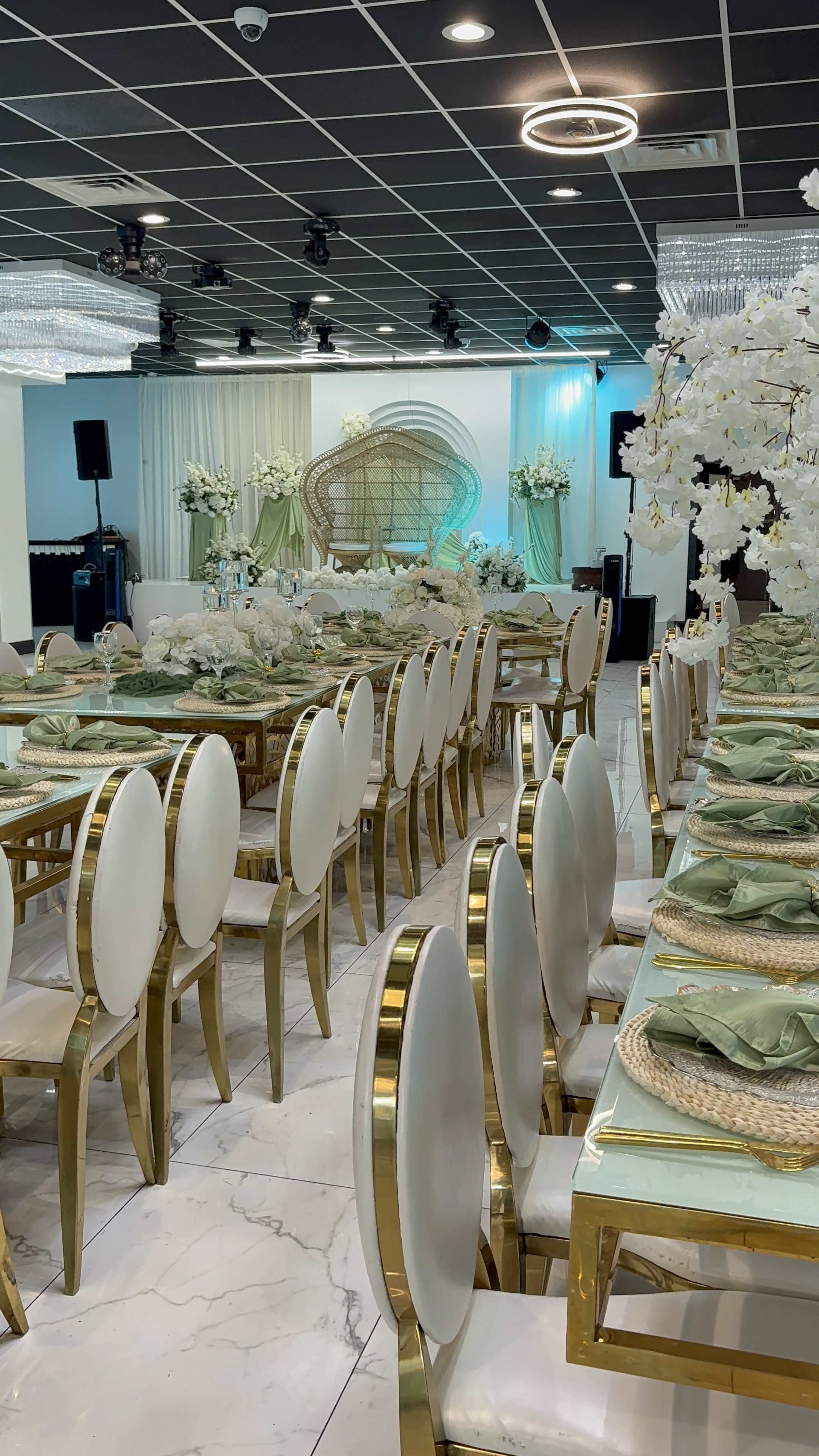 The image shows a decorated banquet hall with white and gold chairs arranged around elegantly set tables featuring green tableware and floral centerpieces.