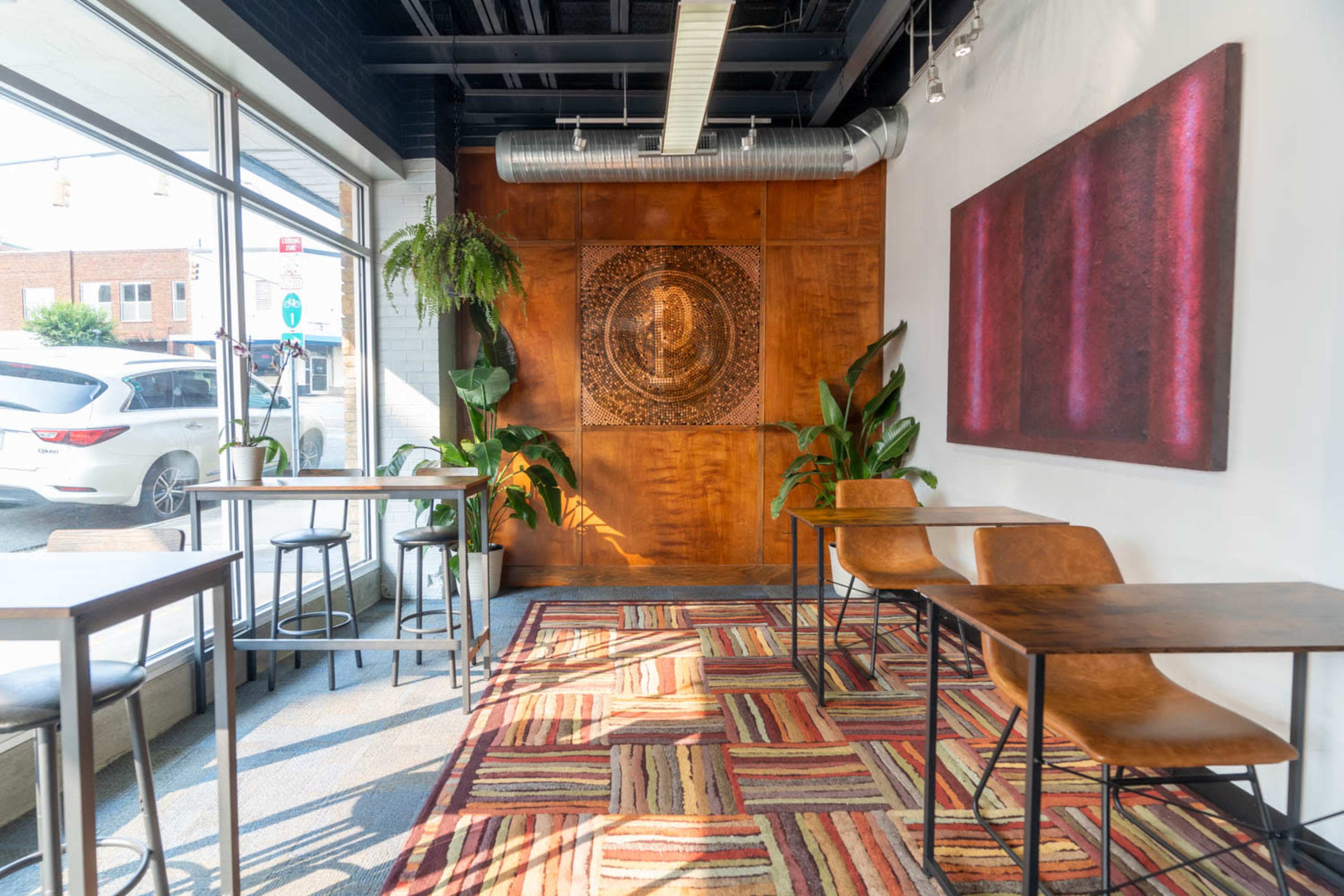 A modern café interior featuring wooden tables and chairs, a colorful striped rug, and a wall with a carved wooden design.