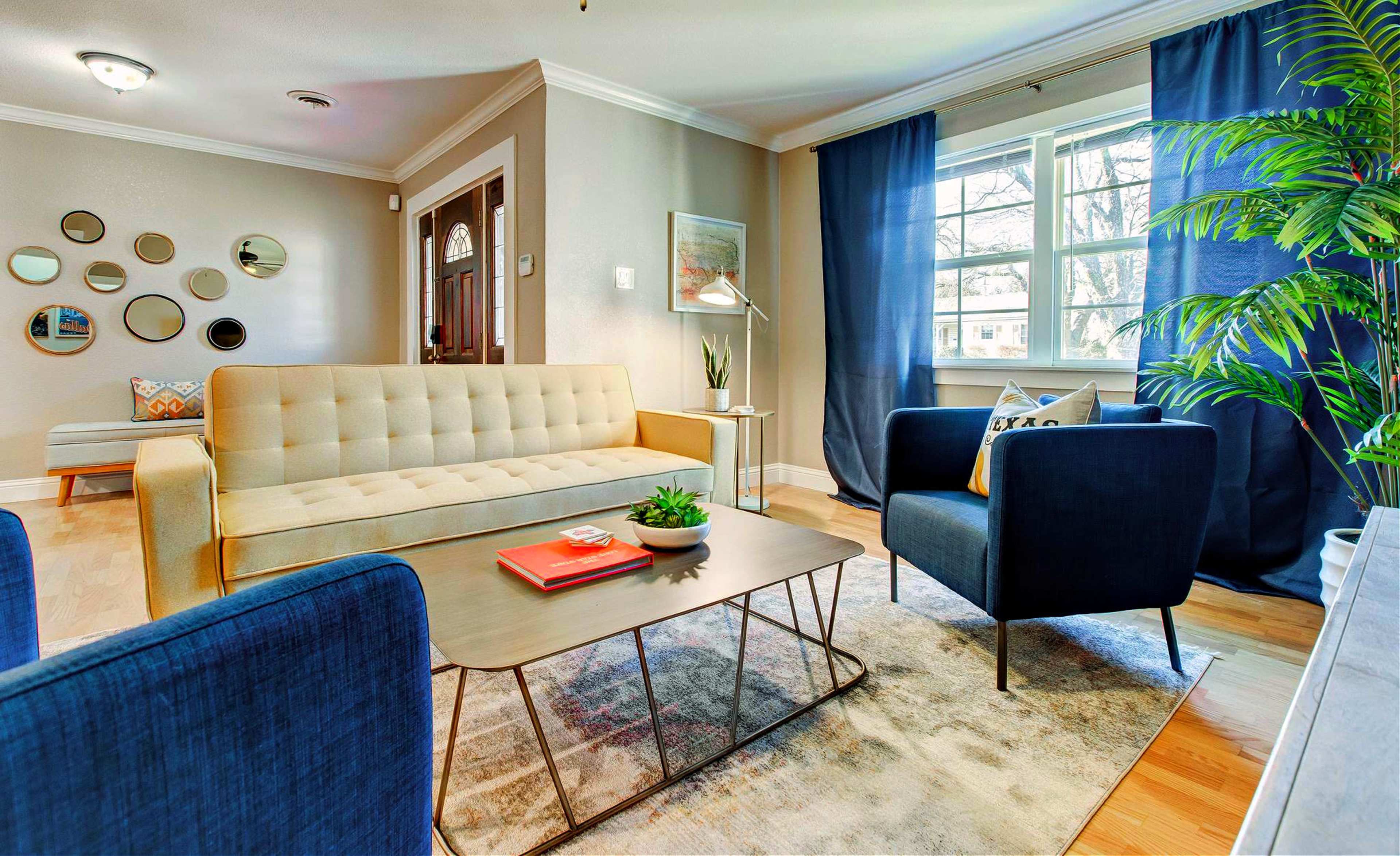 A living room with a beige sofa, two blue armchairs, a coffee table, and large windows covered by dark curtains.