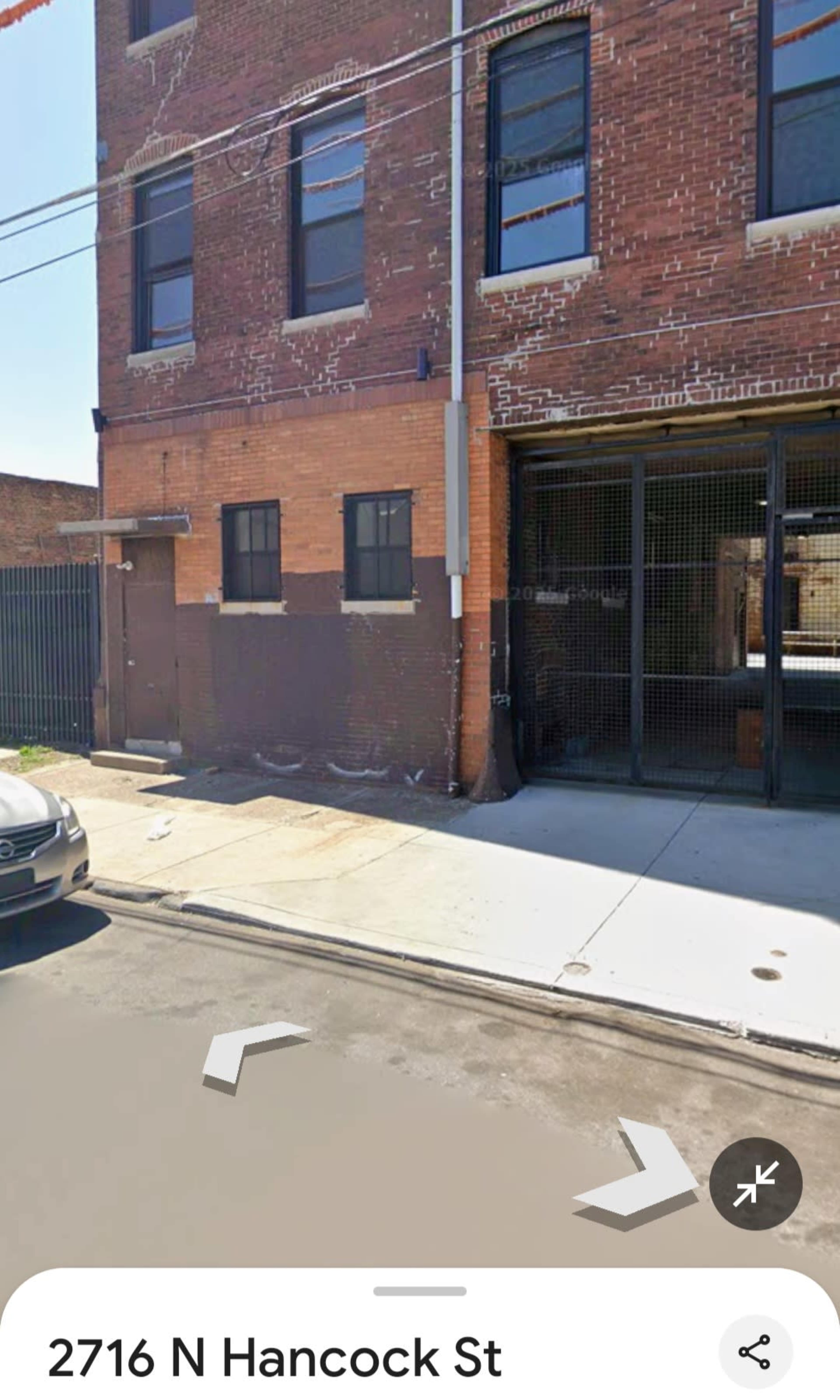The image shows a two-story brick building with a large open garage door on the ground floor, situated at the corner of a street.