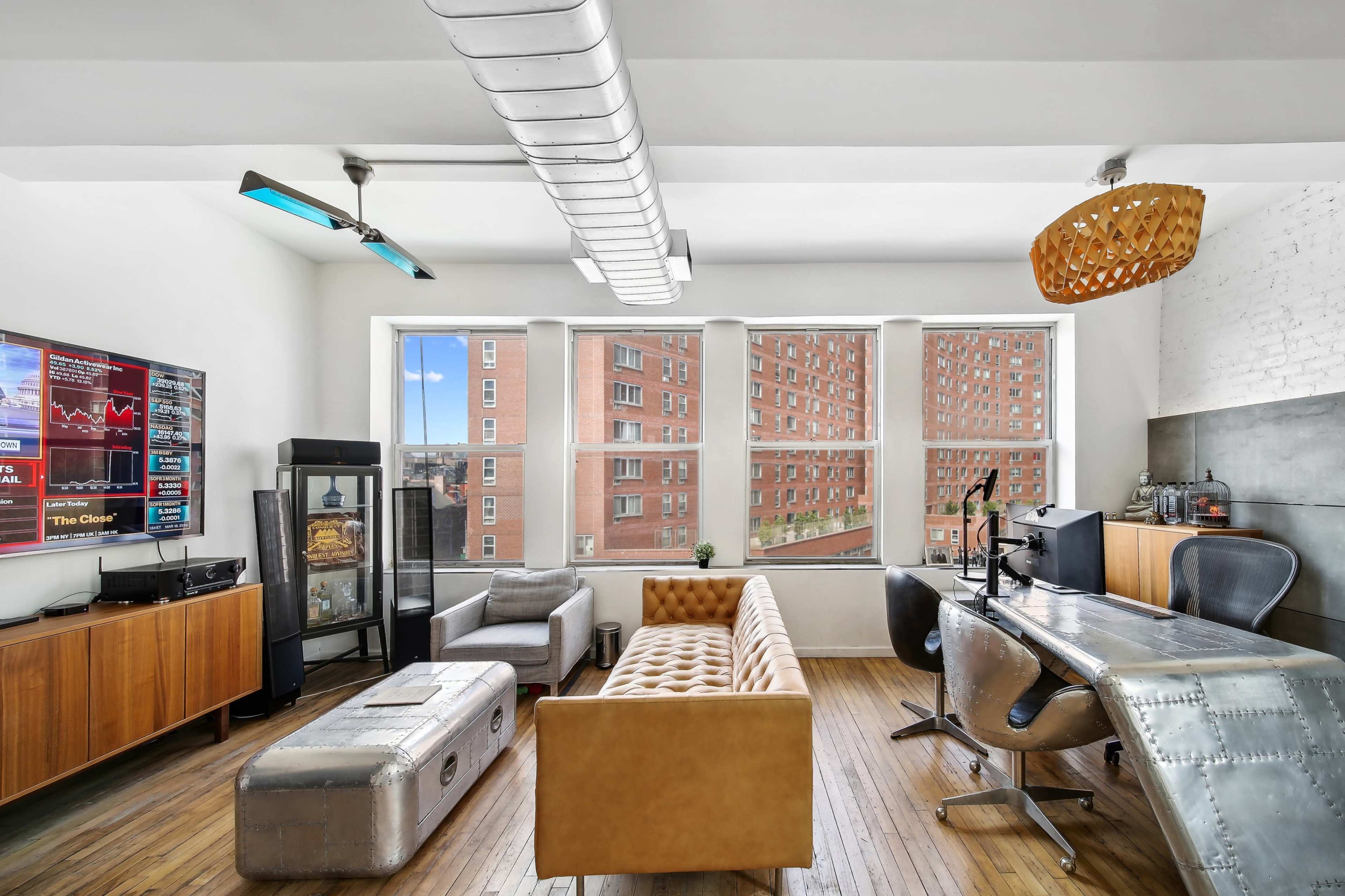 The image depicts a modern office space featuring a leather couch, a metal desk with a computer, large windows with views of buildings, and various decorative elements.