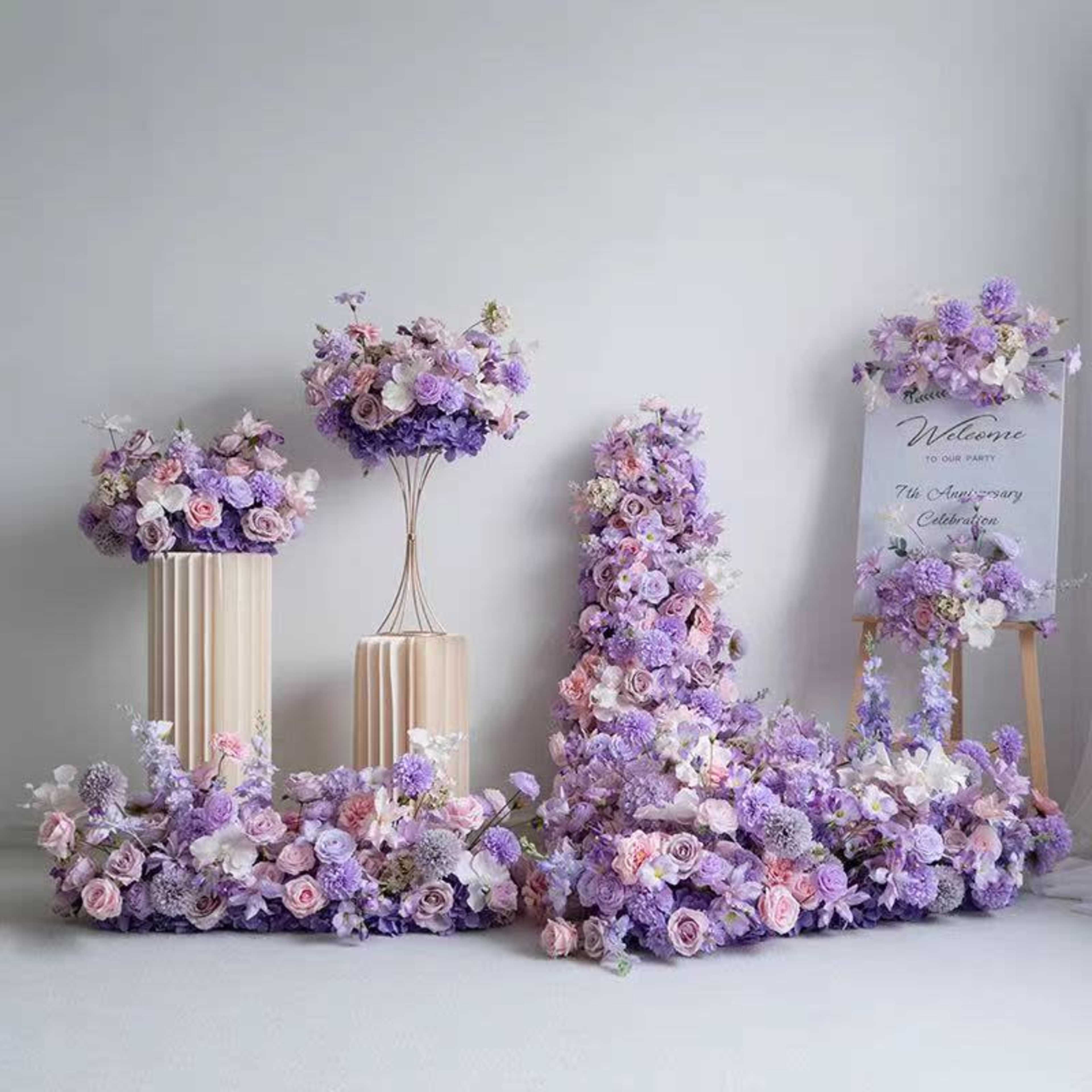 The image features elegant floral arrangements in shades of purple and pink, including large letters and a welcome sign, set against a neutral backdrop.
