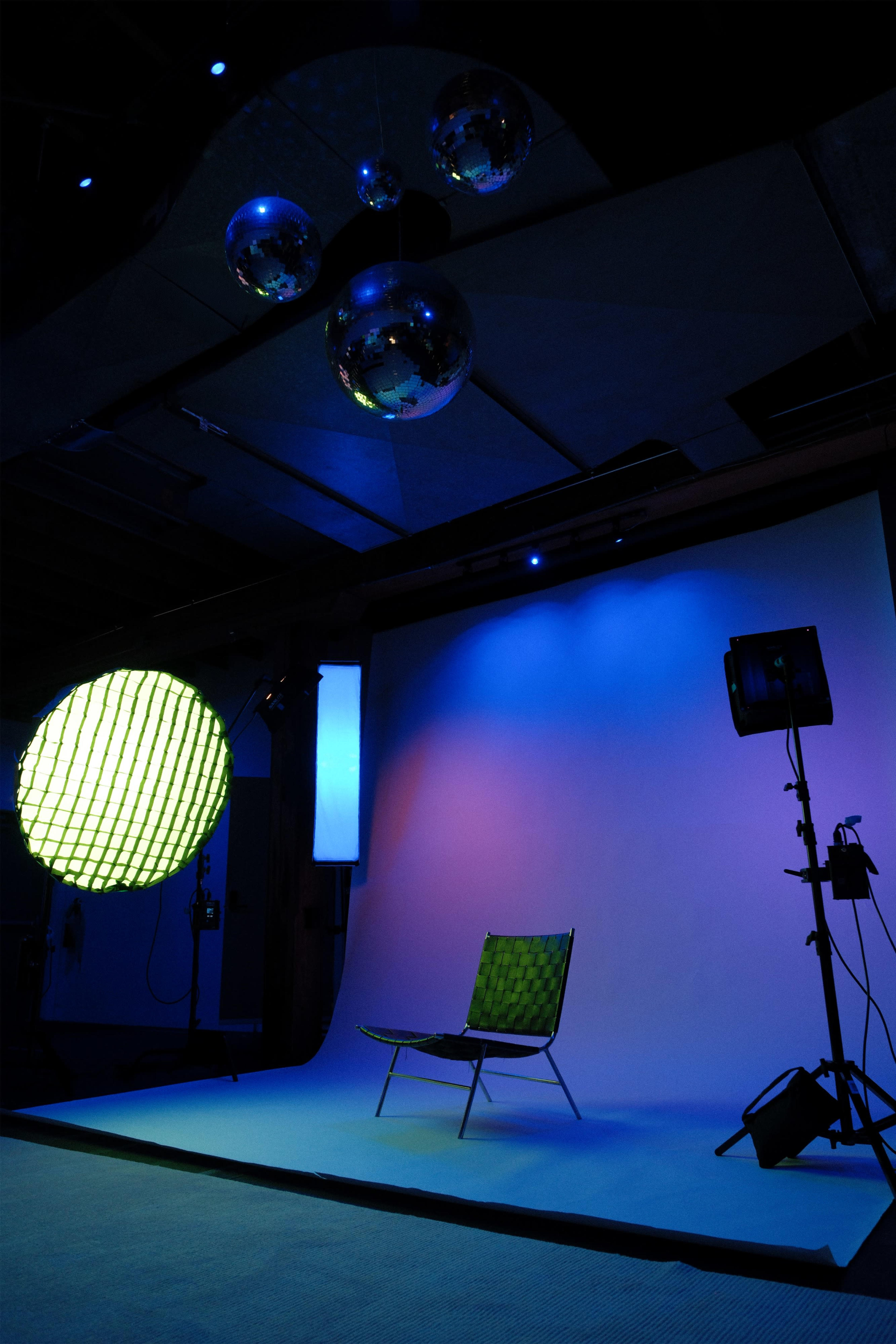 The image shows a studio setup featuring a checkered chair, colorful background lights, and hanging disco balls.