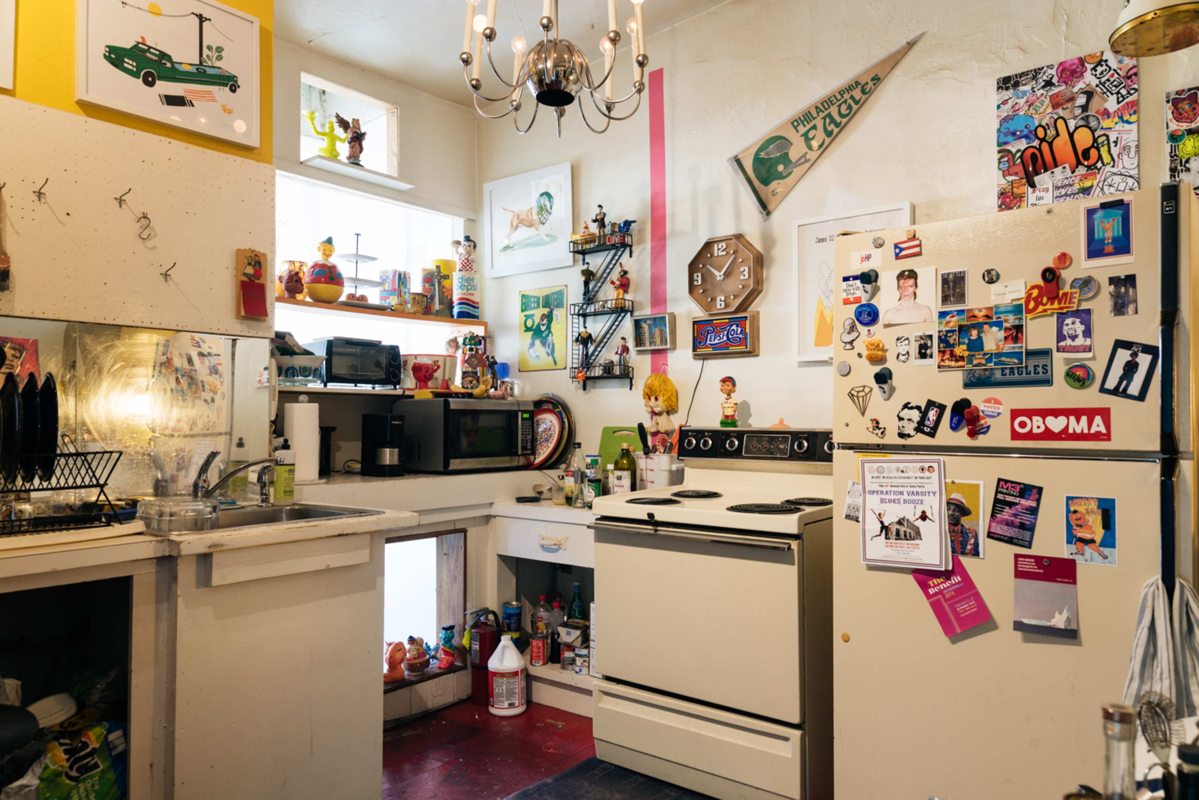 A small, eclectic kitchen is filled with colorful decorations, appliances, and various items adorning the walls and refrigerator.