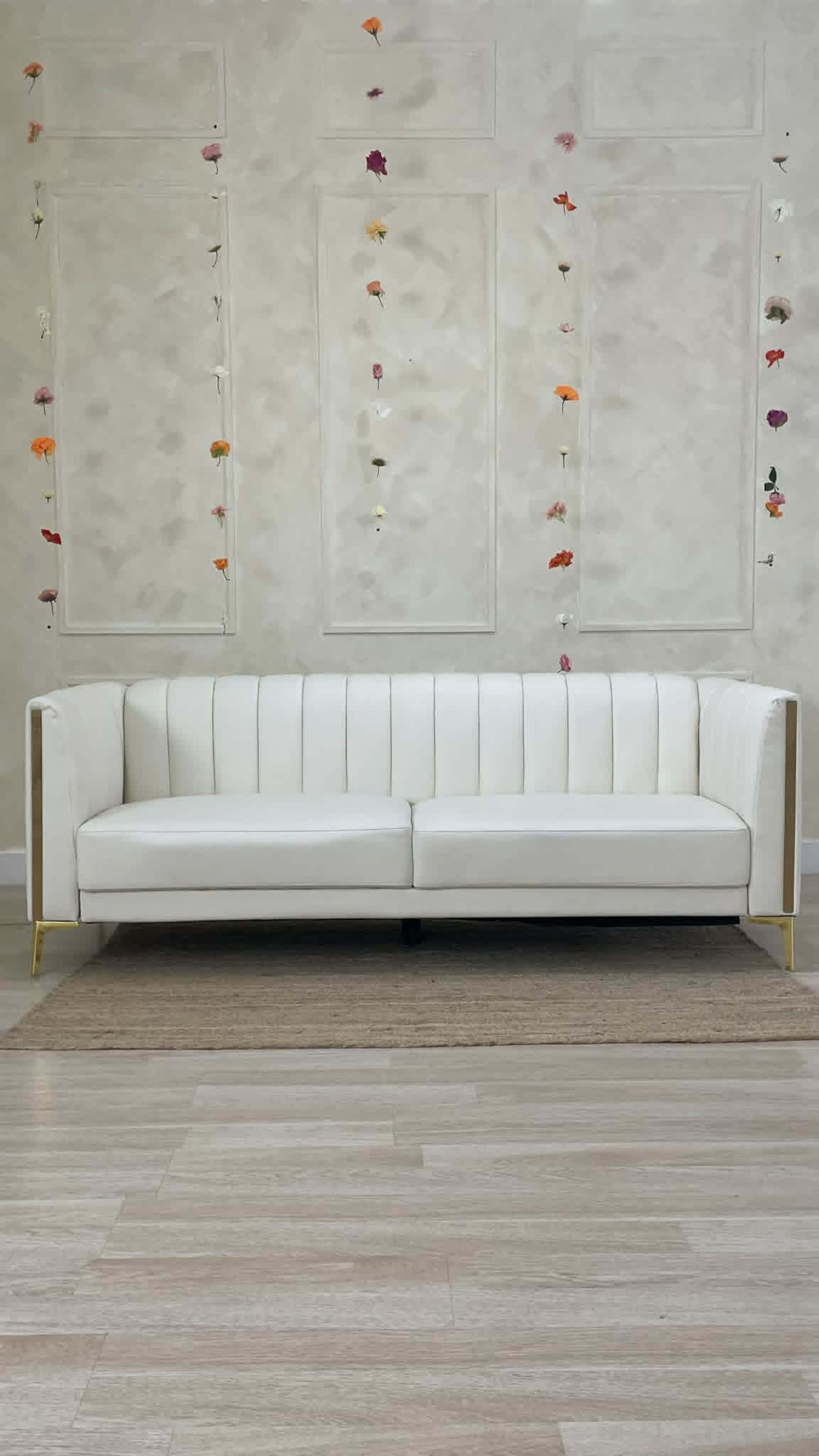 A white, modern upholstered sofa is positioned in front of a wall adorned with colorful flower decorations.
