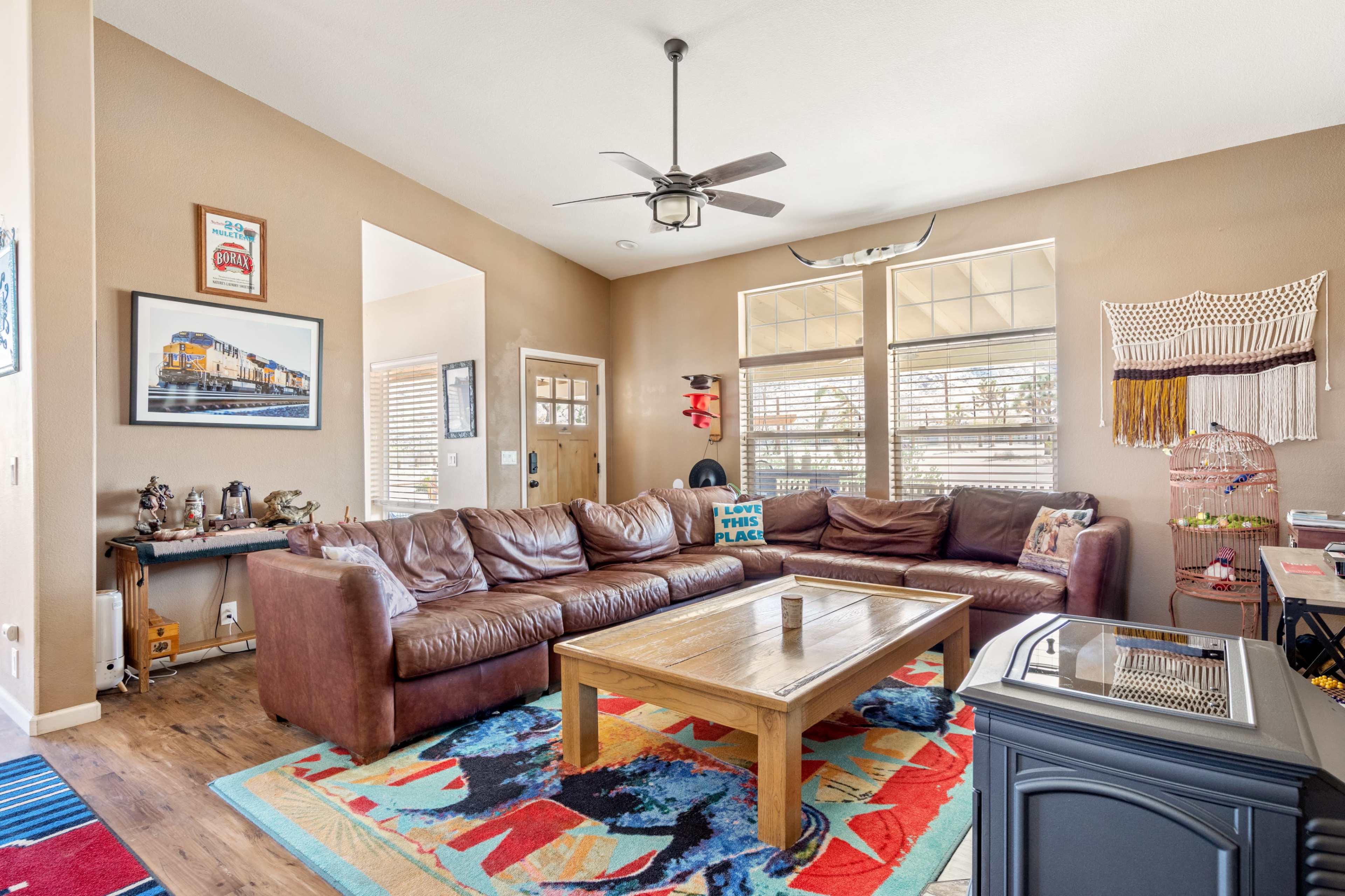 A living room with a large brown leather sectional sofa, a wooden coffee table, and colorful area rugs on the floor.