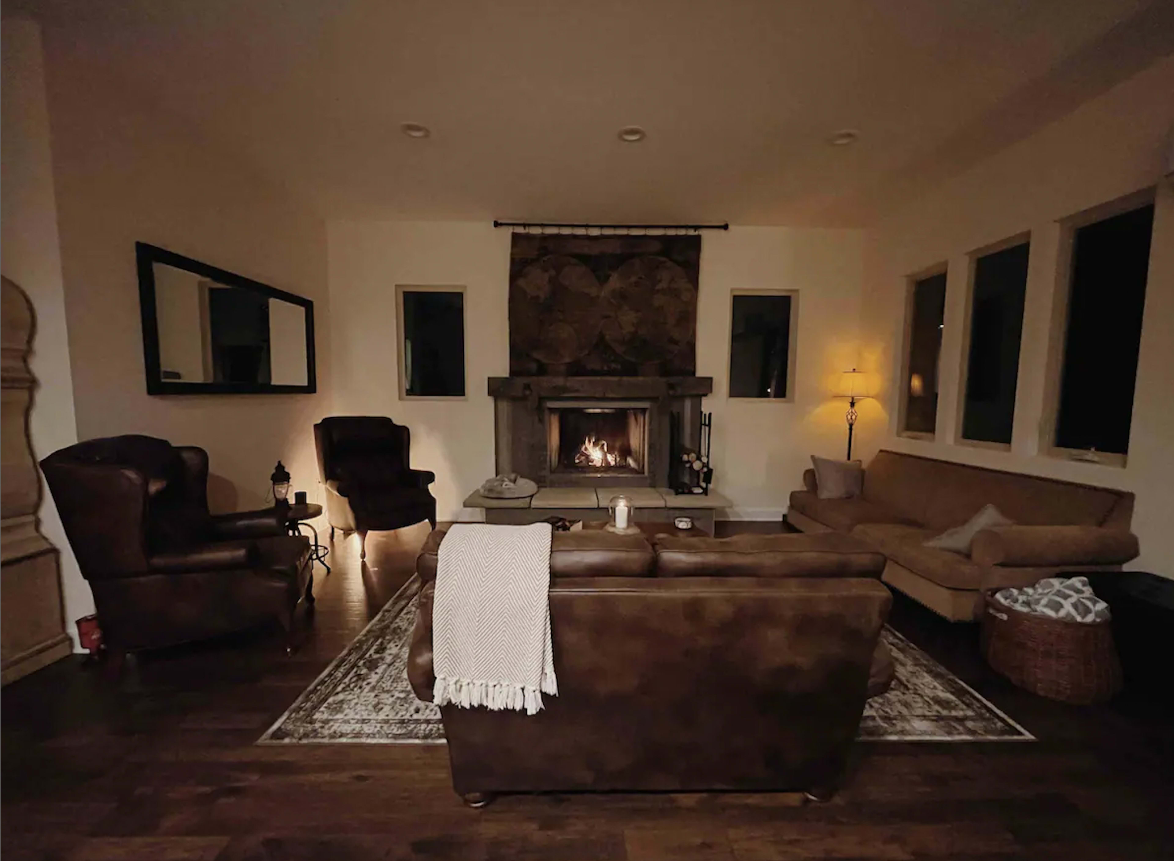 A cozy living room features a stone fireplace, two armchairs, a couch, and a coffee table, all arranged on wooden flooring.