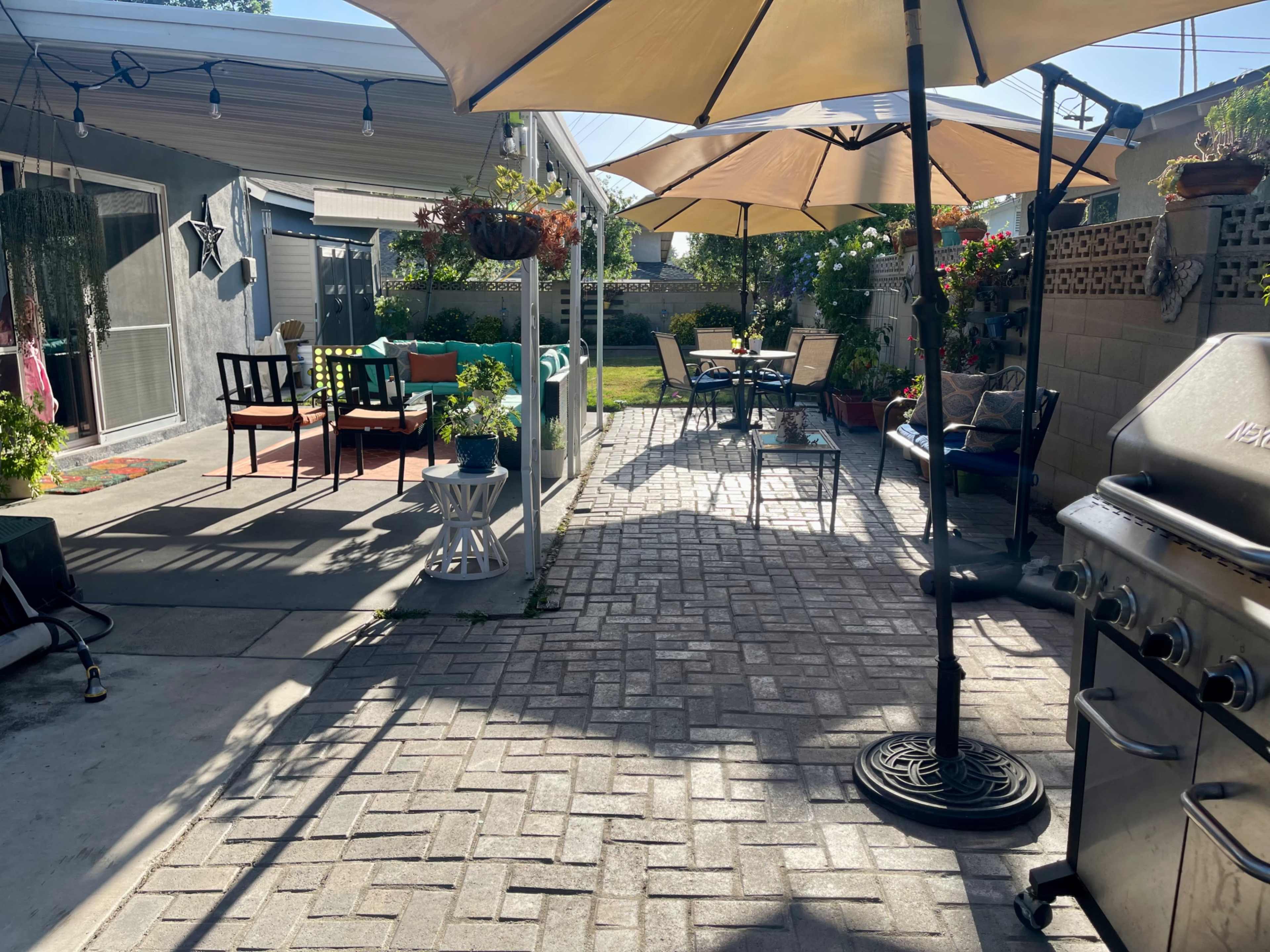 A patio area with outdoor furniture, two large umbrellas, potted plants, and a grill.