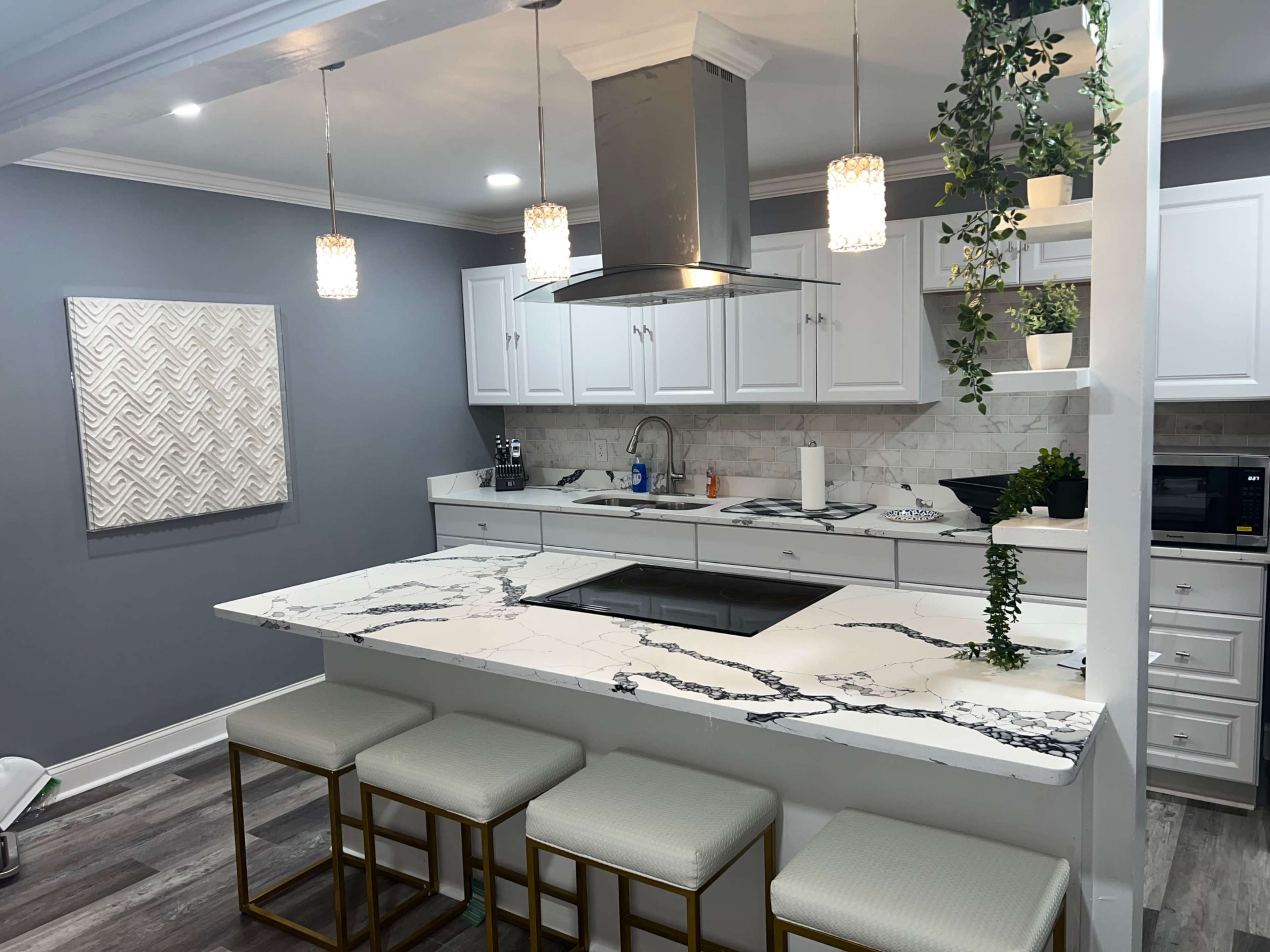 A modern kitchen featuring a marble island with bar stools, white cabinets, and a stainless steel vent hood above the stove.