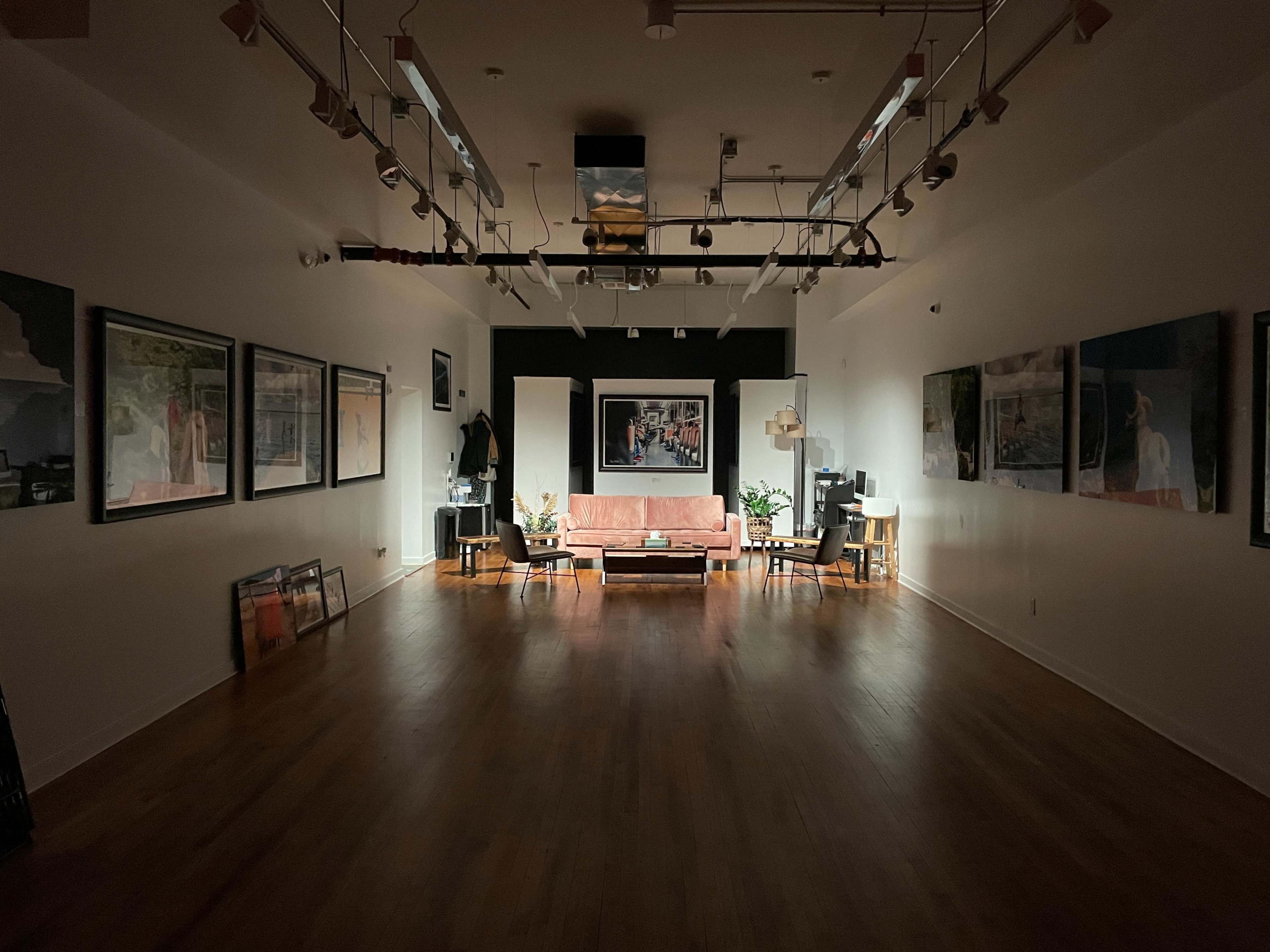 A spacious gallery features framed artworks on the walls, with a sofa and coffee table in the center, illuminated by overhead lighting.