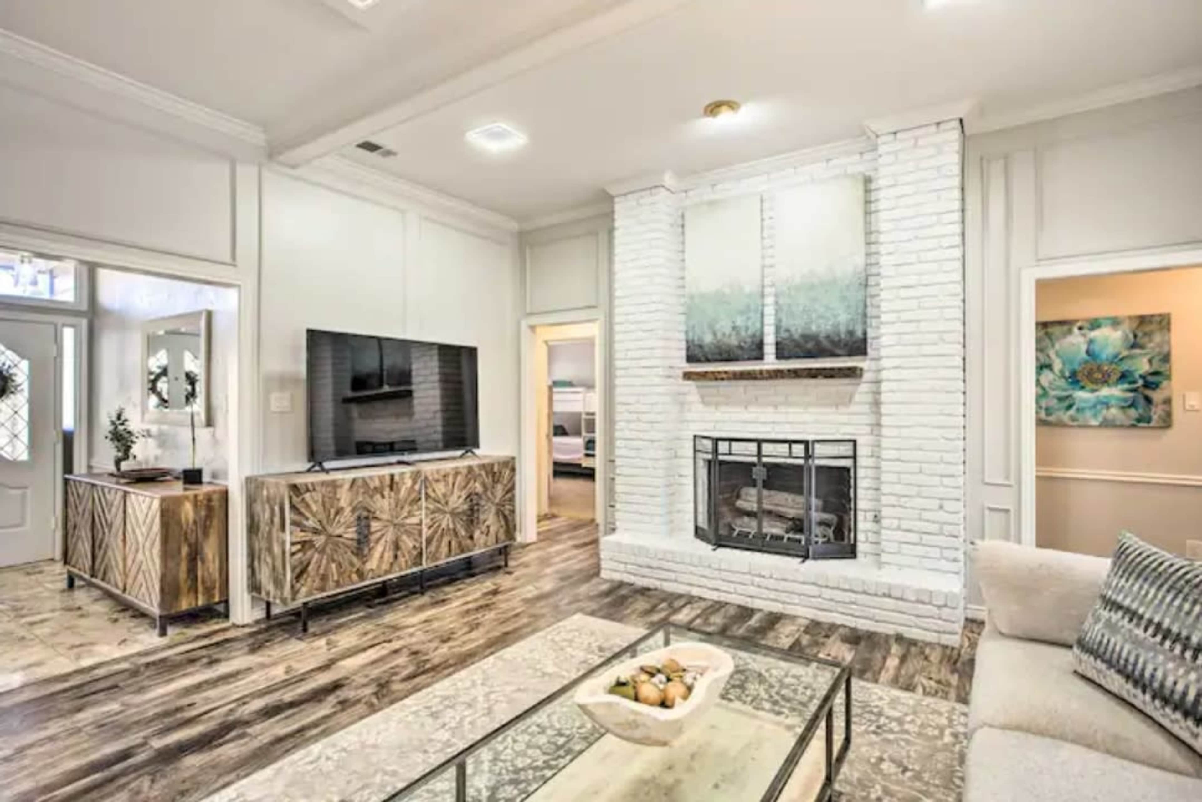 The living room features a white brick fireplace, a television mounted on the wall, and a light-colored sofa, with a wooden console and decorative artwork present.