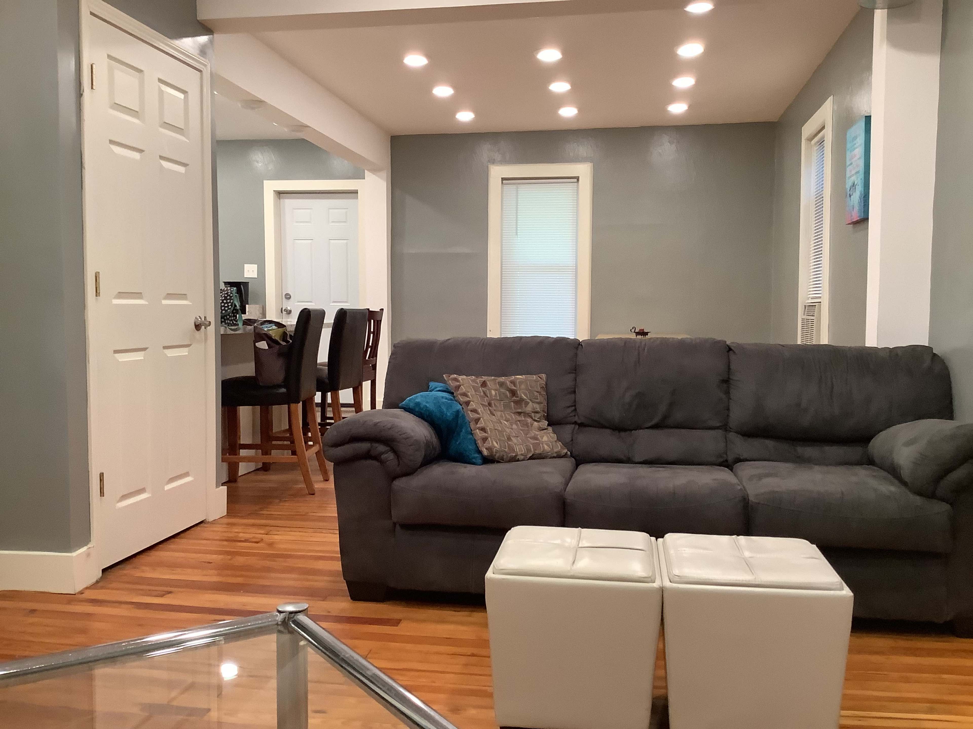 A living room with a gray couch, a glass coffee table, and a view of a dining area in the background.