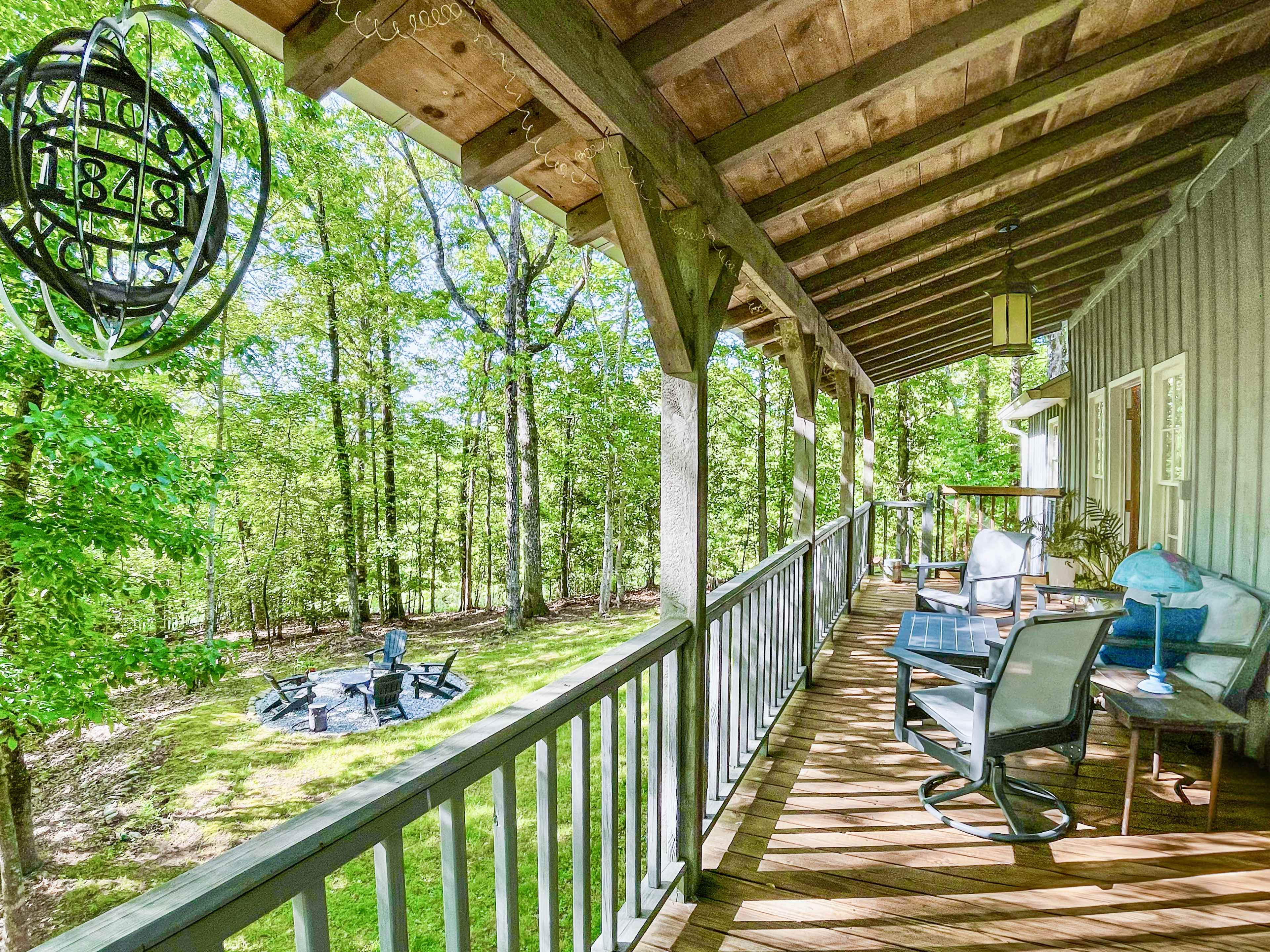 A wooden porch with rocking chairs overlooks a fire pit surrounded by trees in a natural setting.