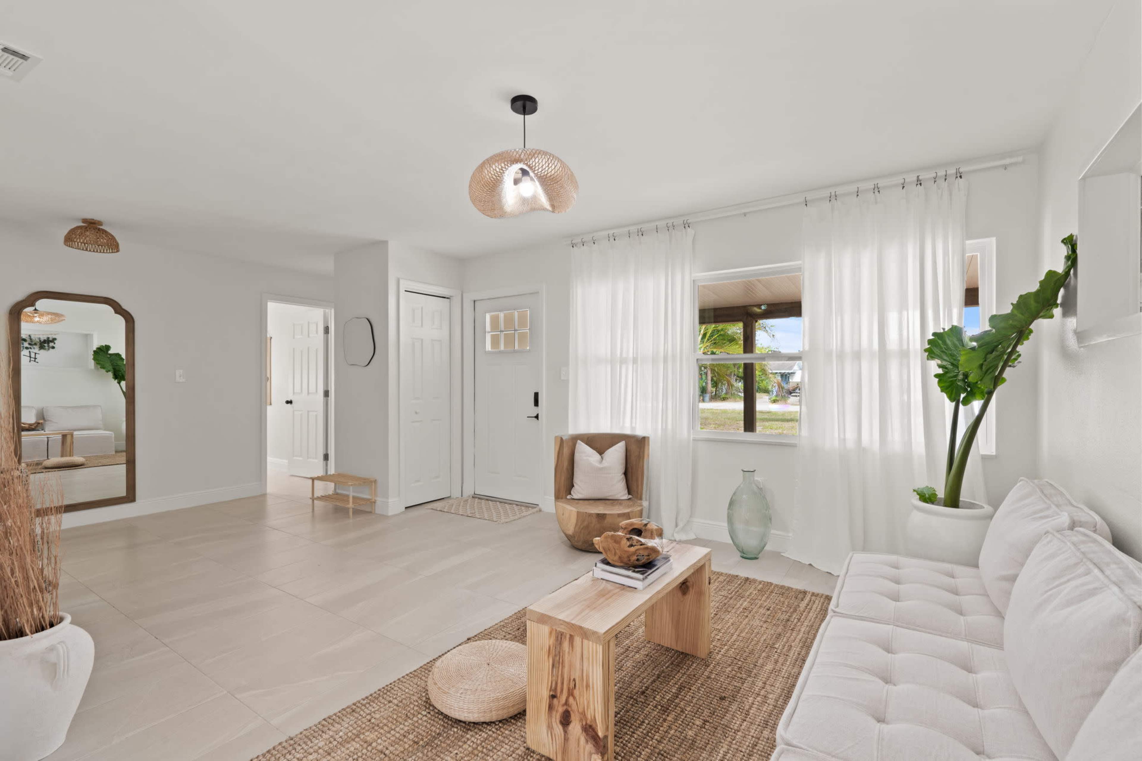 A light and airy living room featuring a white sofa, a wooden coffee table, and large windows with sheer curtains.