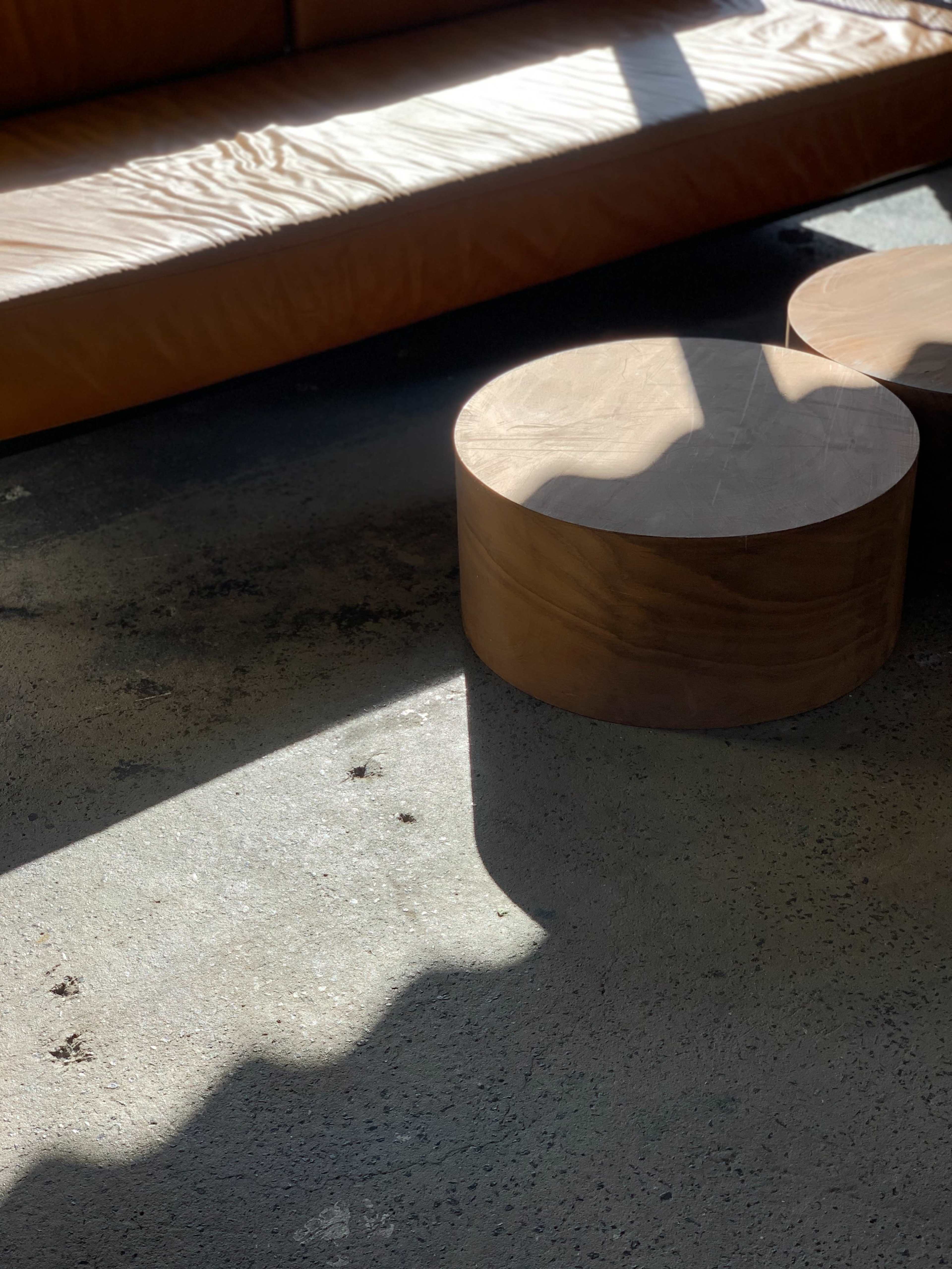 A low wooden table sits on a textured floor beside a sunlit leather sofa.