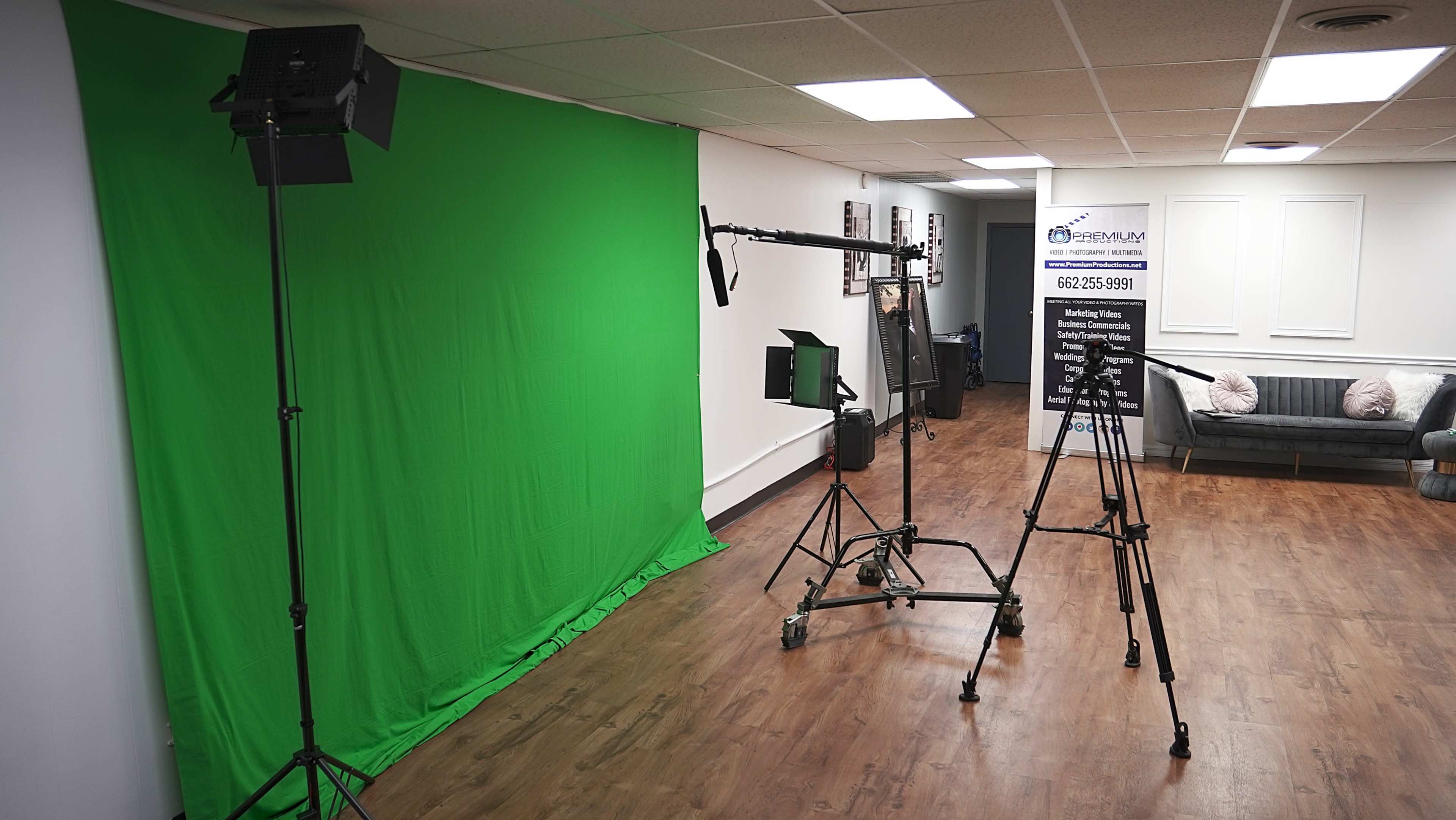 The image shows a film studio setup featuring a green screen, lighting equipment, a camera on a tripod, and a backdrop with text on display.