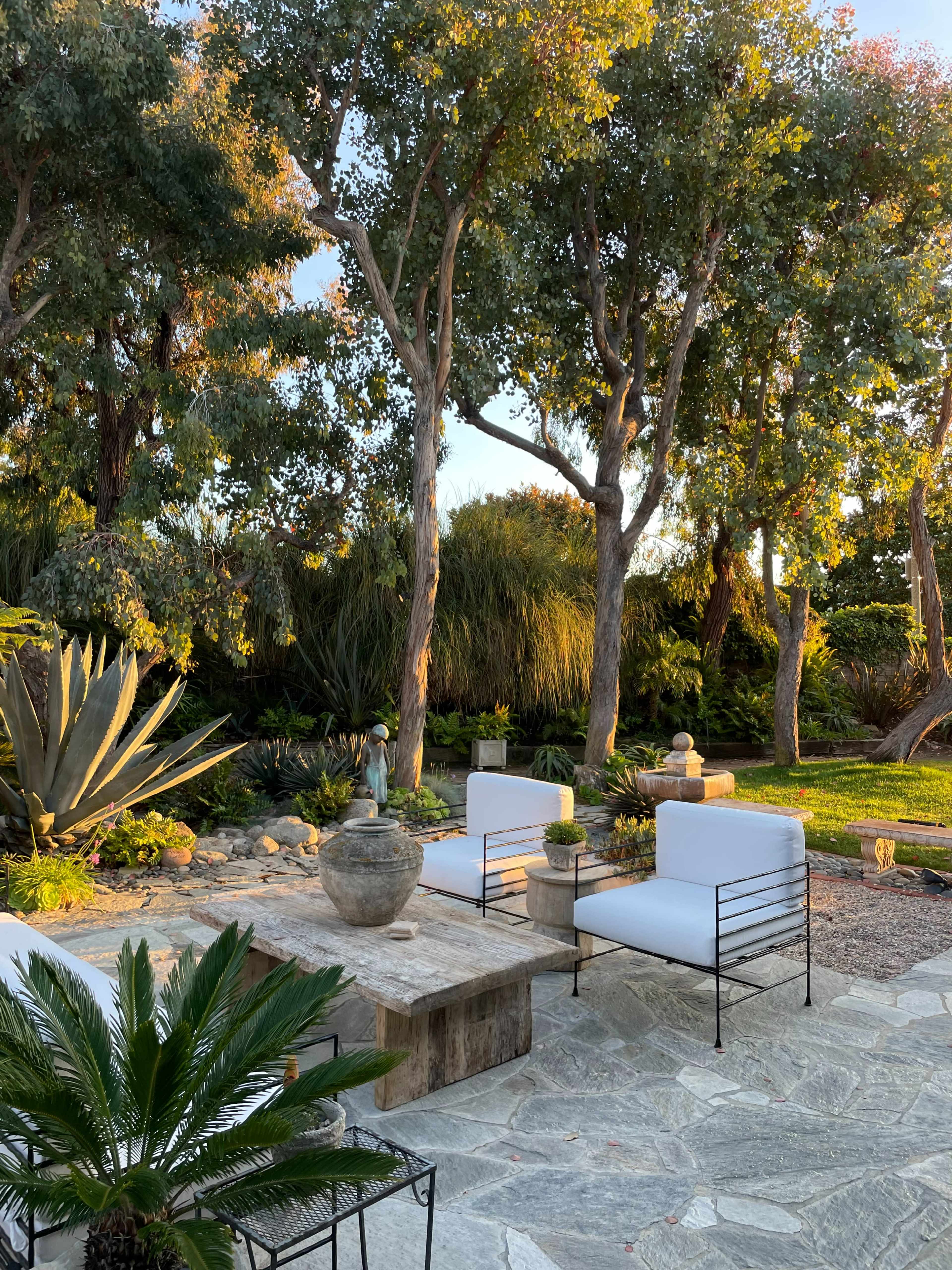 A landscaped outdoor area with stone seating, potted plants, and surrounded by tall trees.