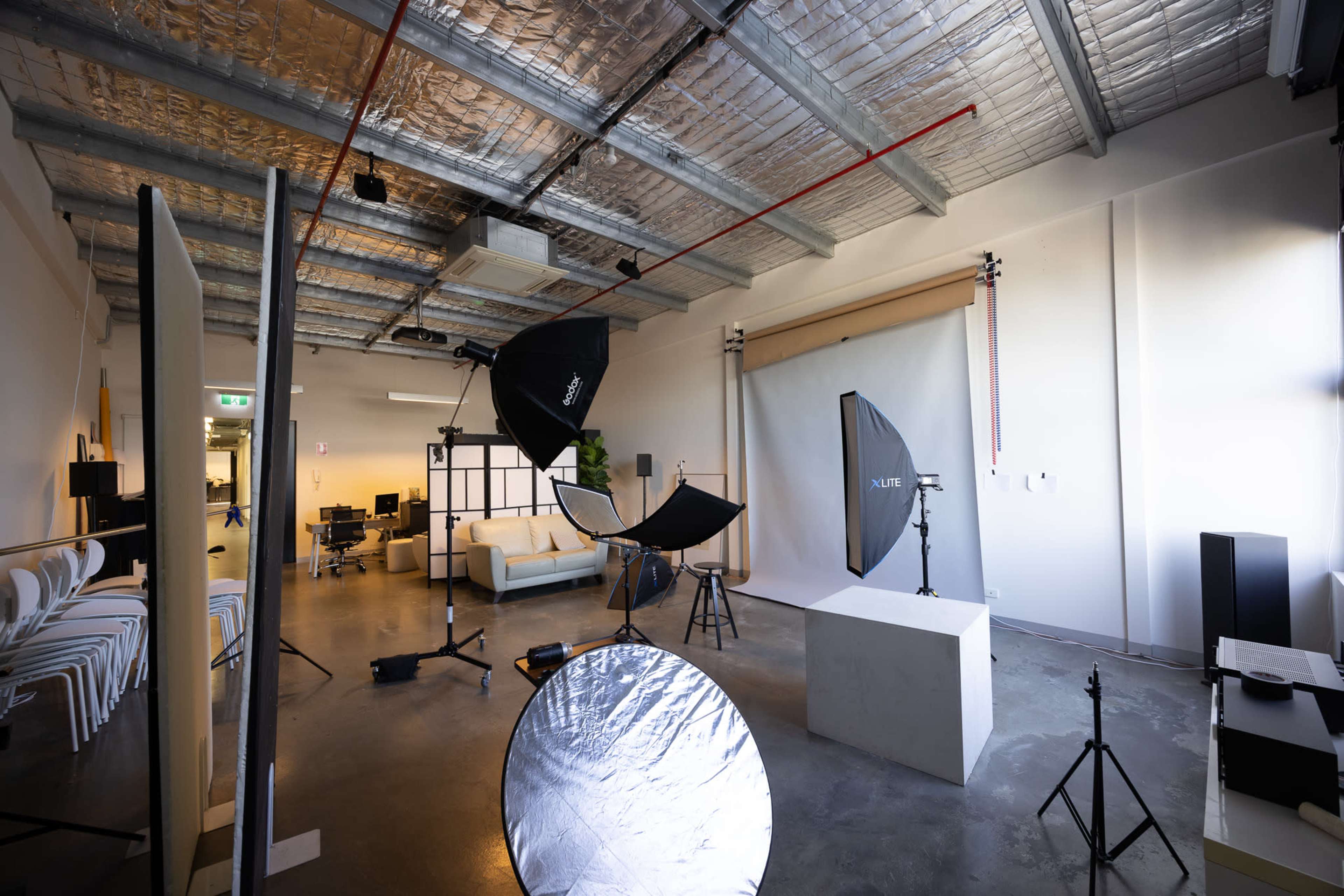 The image depicts a spacious photography studio equipped with various lighting equipment, backdrops, and seating arrangements.