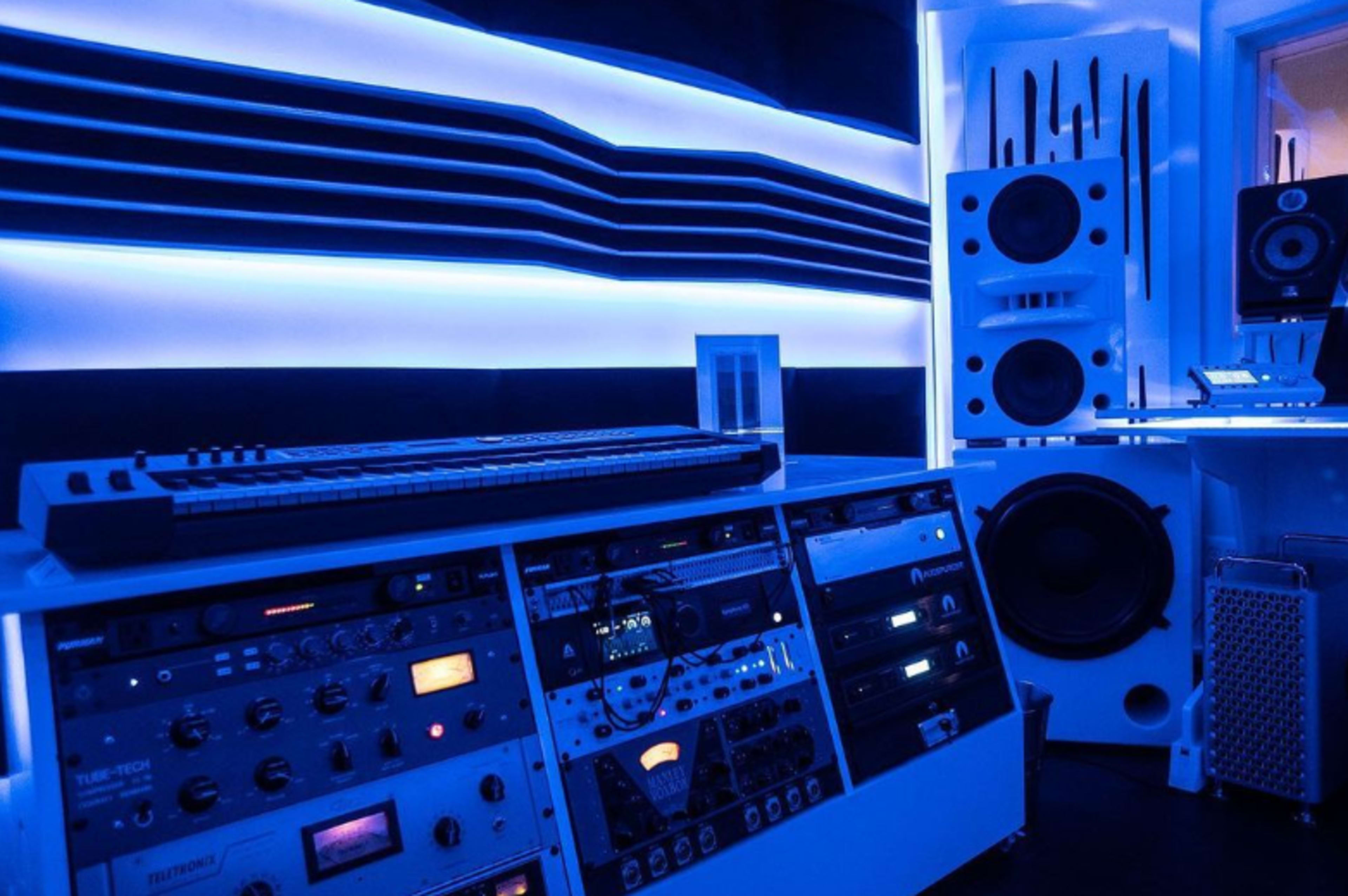 A modern music studio with a keyboard, audio equipment, and blue LED lighting.
