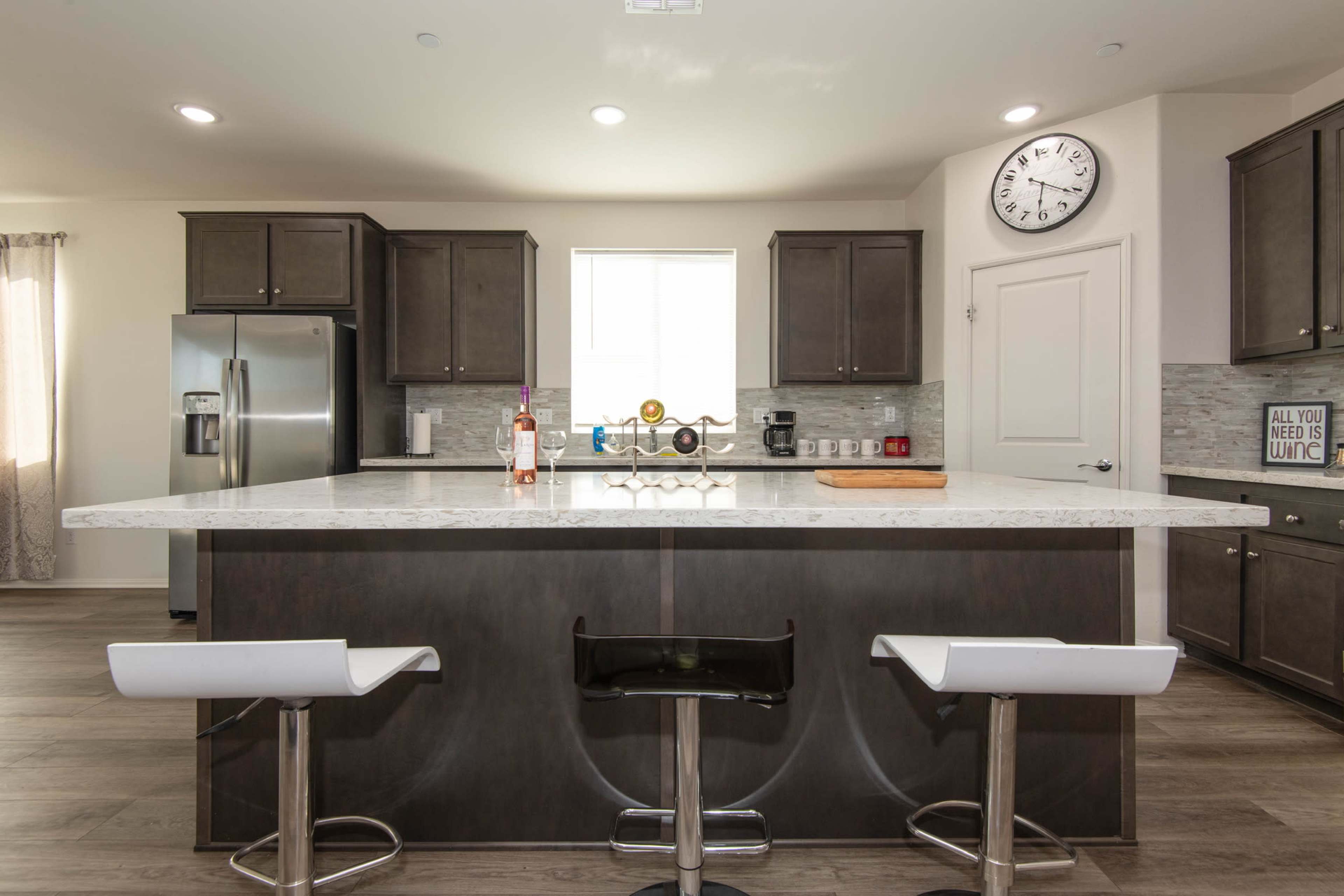 The kitchen features dark cabinetry, a large marble island with bar stools, and stainless steel appliances.