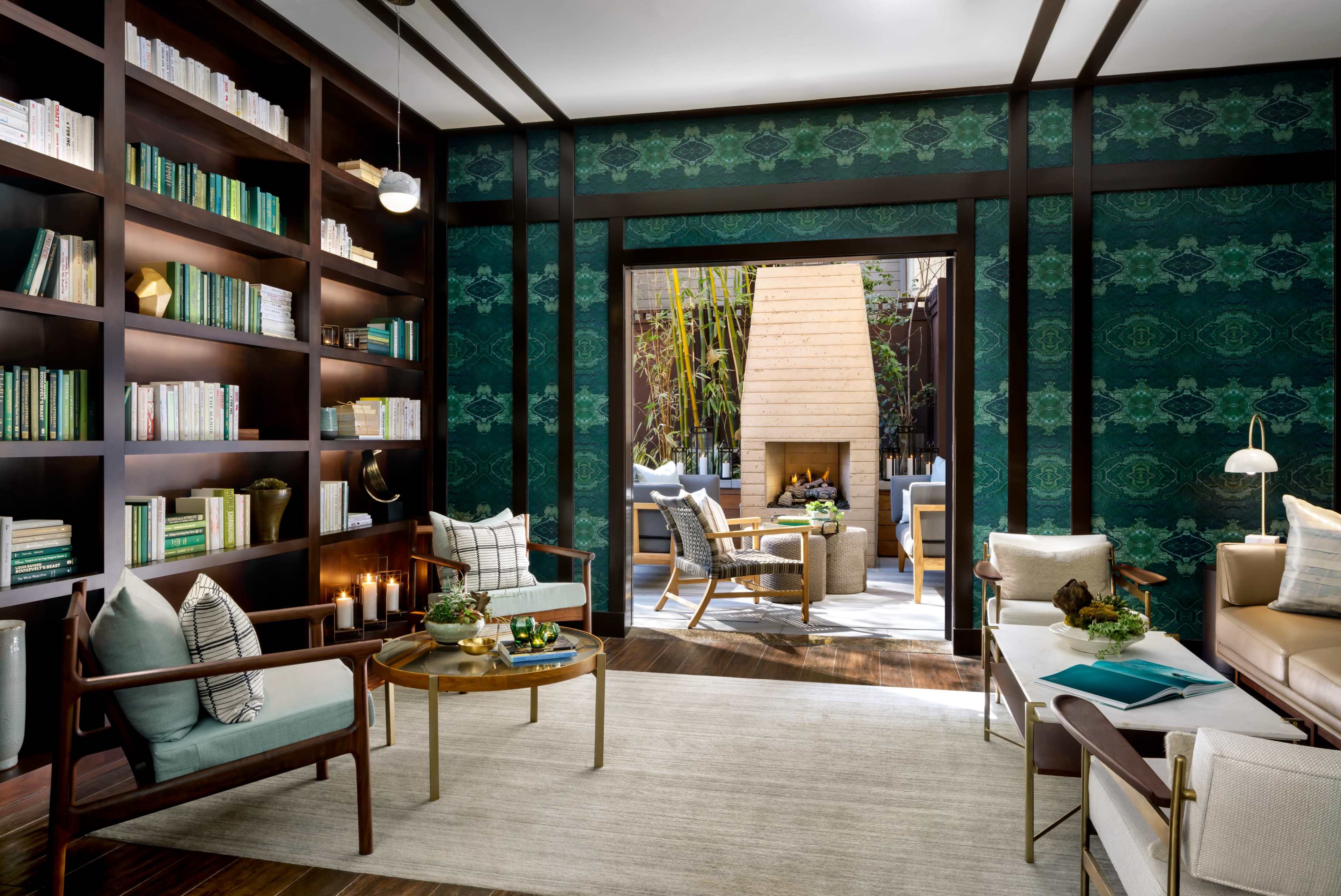 A modern library area features a built-in bookshelf filled with books, a cozy seating arrangement, and a view of an outdoor space with a fireplace.
