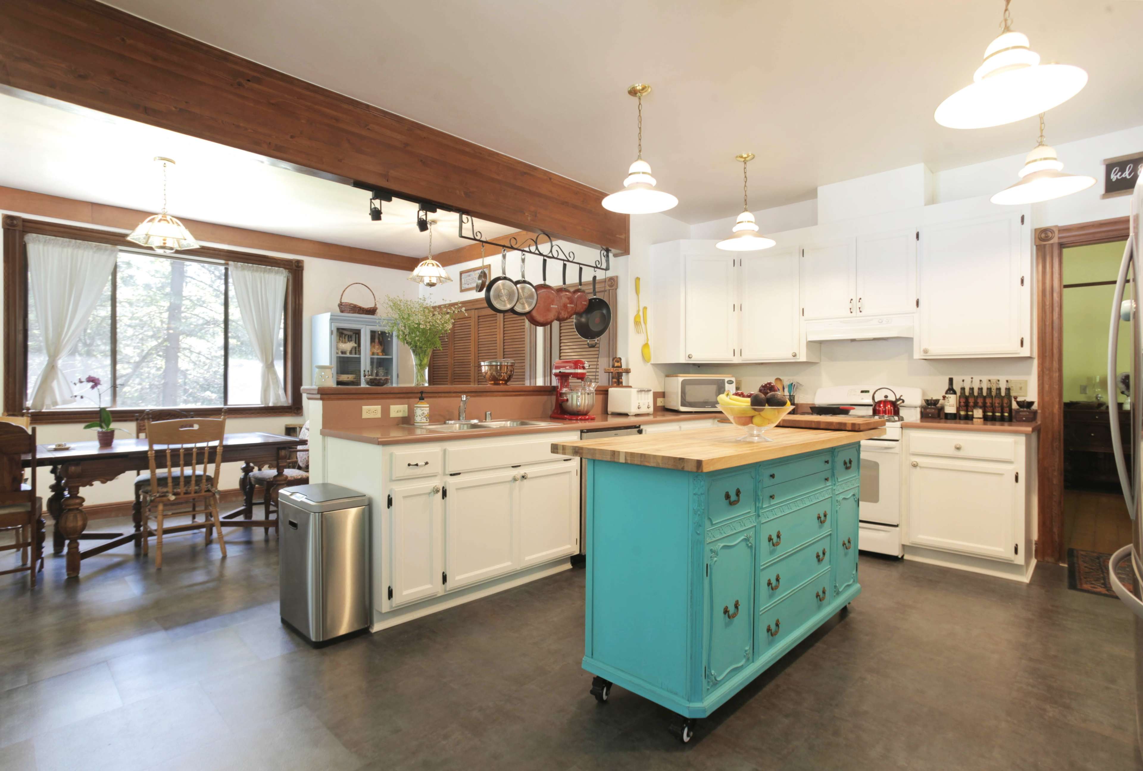 The kitchen features white cabinetry, a central turquoise island, and a dining area with a wooden table and chairs.