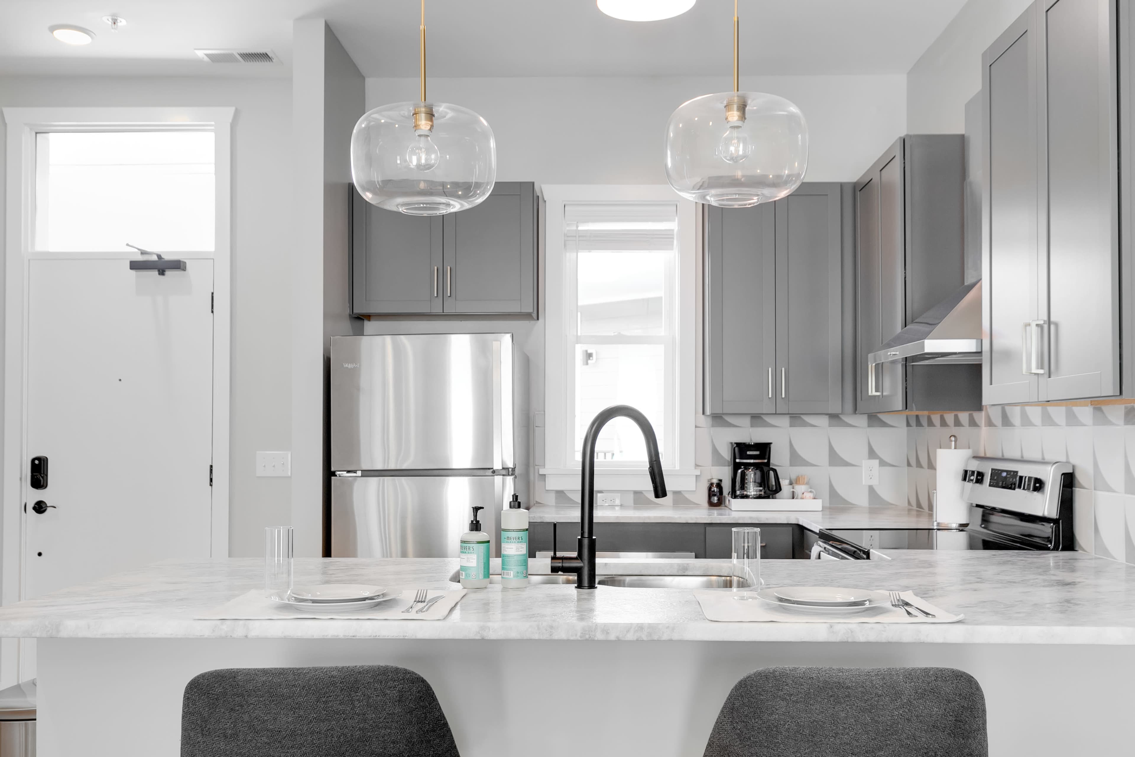 A modern kitchen with gray cabinets, stainless steel appliances, and a marble island featuring two gray chairs.