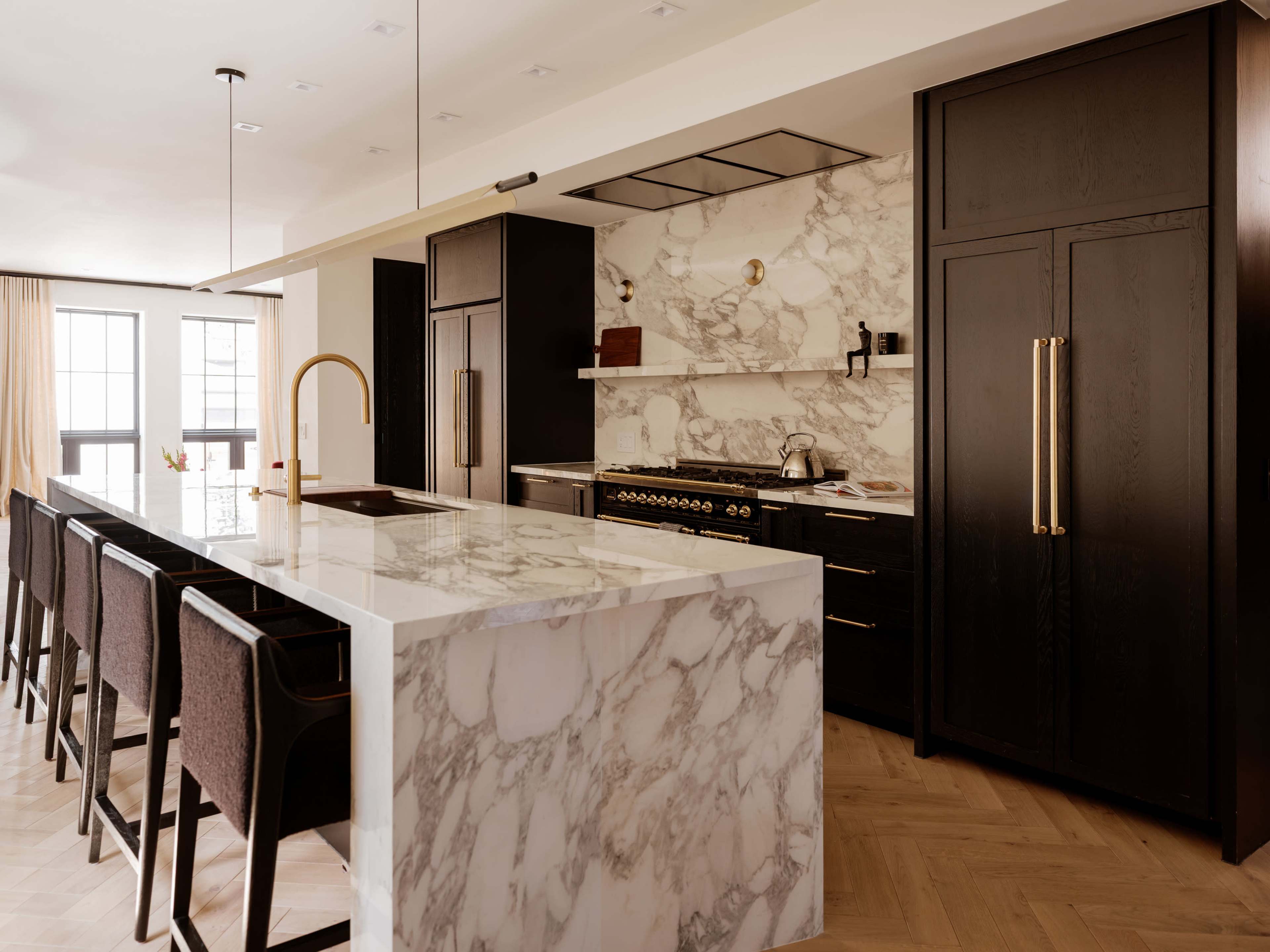 The kitchen features a large marble island with a sink and bar seating, surrounded by dark cabinetry and modern appliances.