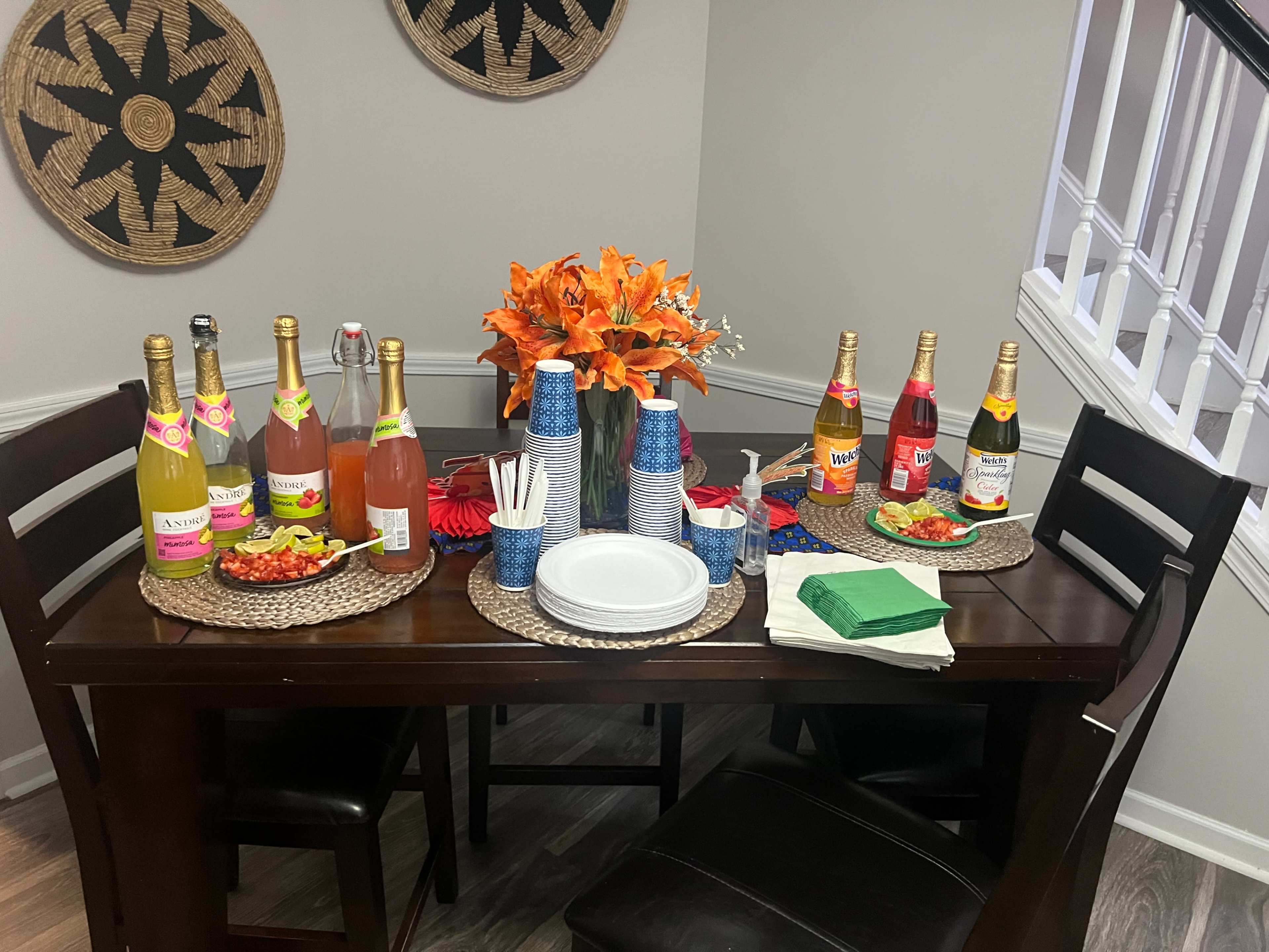 A table is set with colorful drinks, snacks, and decorative flowers, surrounded by chairs in a cozy dining area.