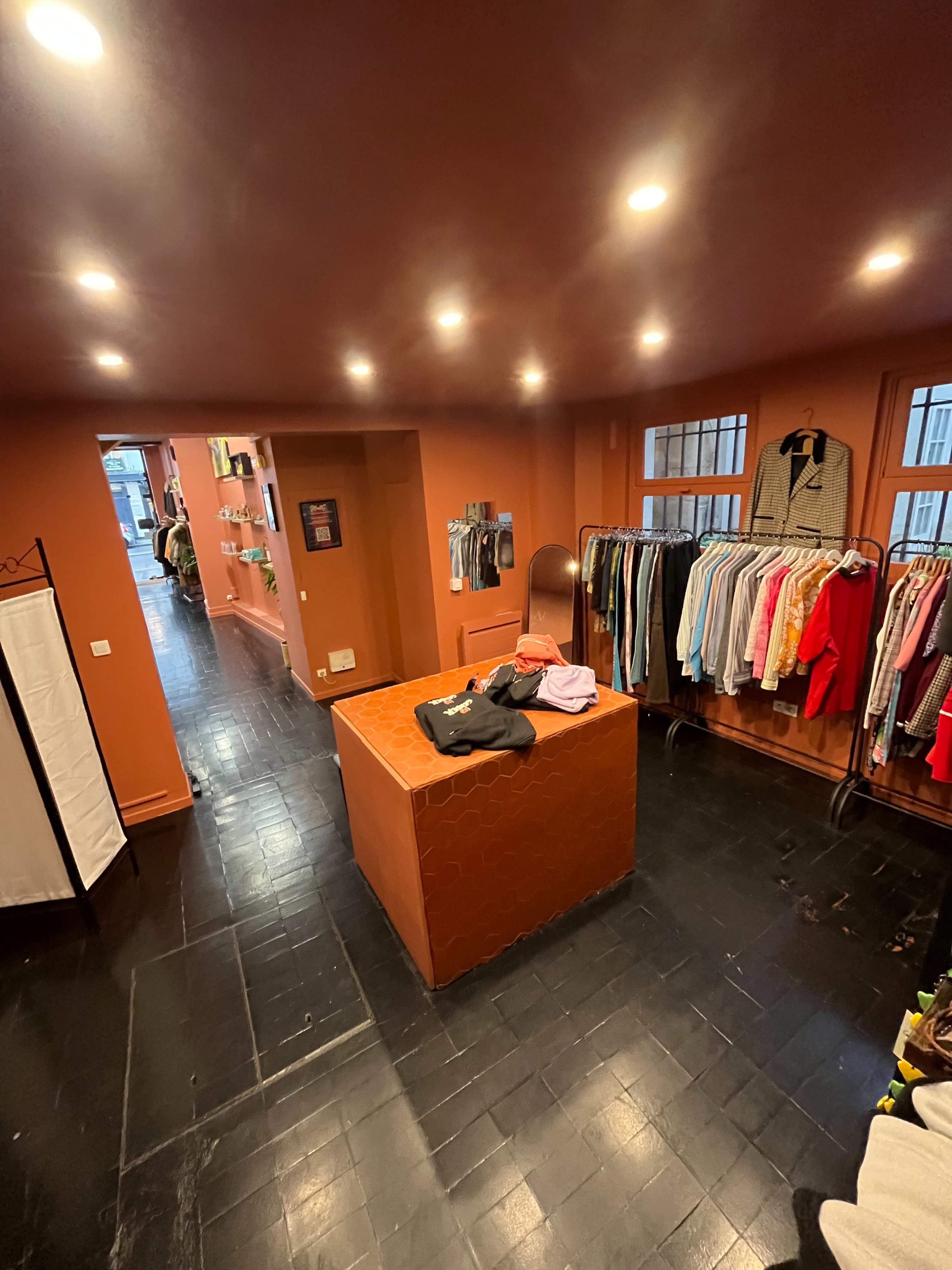 A boutique interior featuring a central display table and clothing racks along the walls, all set against a warm, colored backdrop.