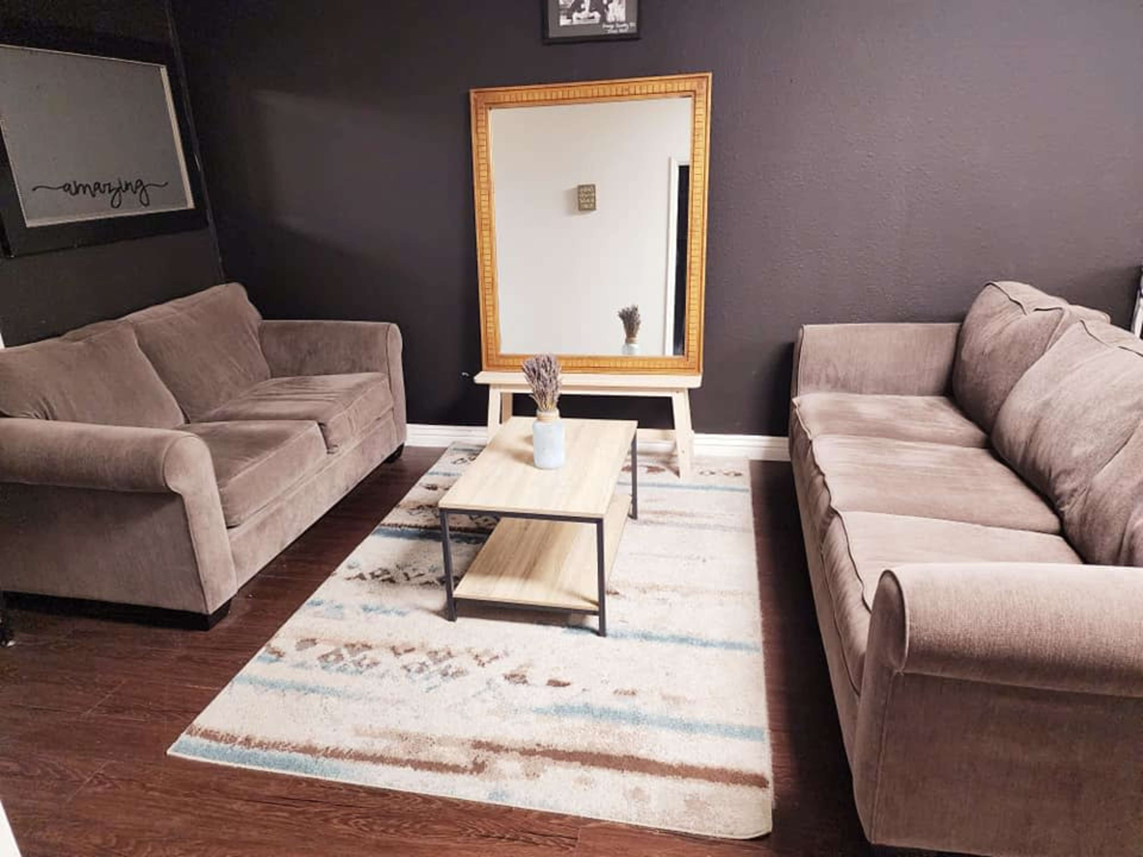 A cozy living room with two gray sofas facing each other, a wooden coffee table in the center, and a large mirror on the wall.