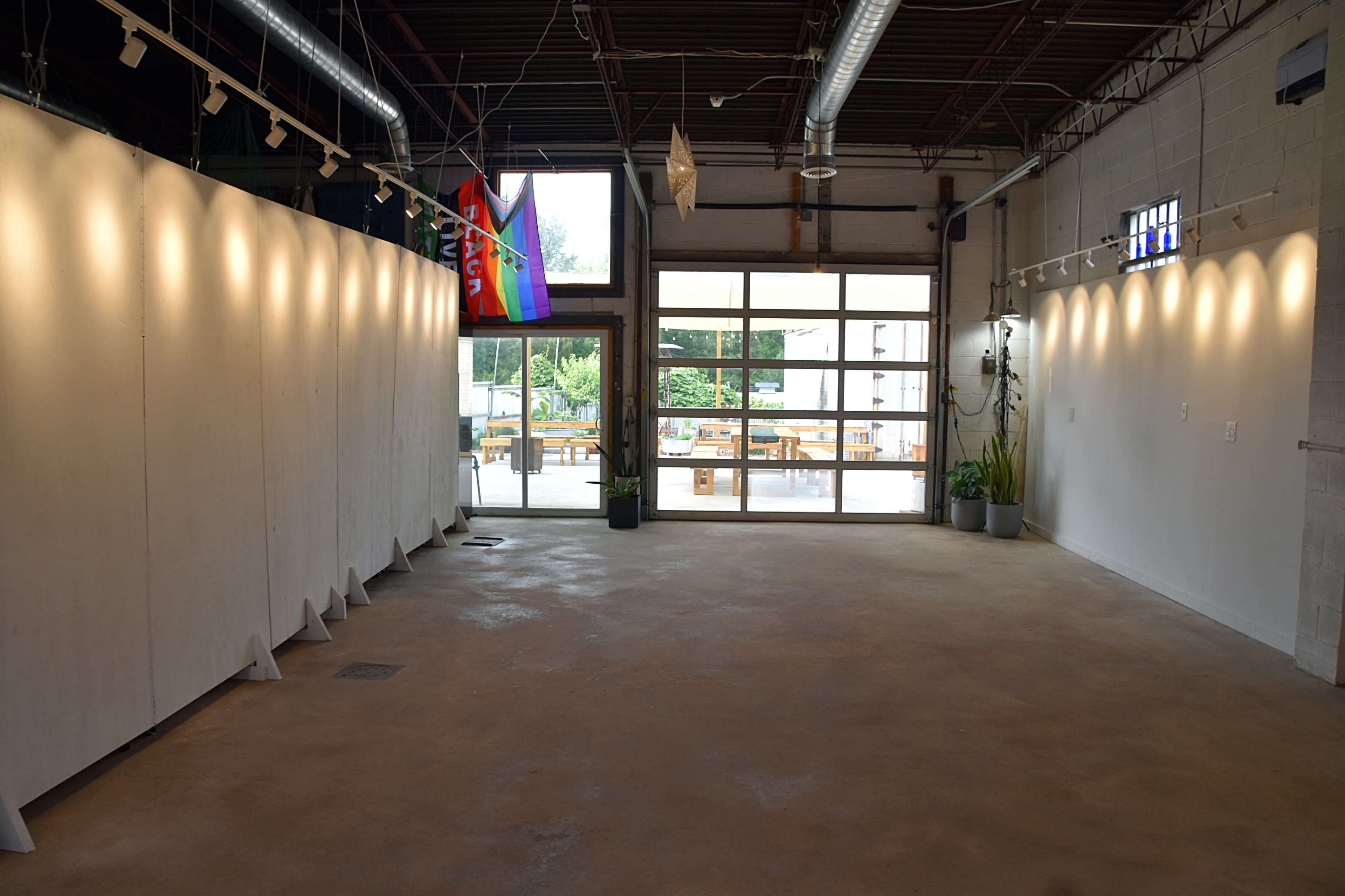 An empty interior space with white walls, large windows, and a patio area visible outside.