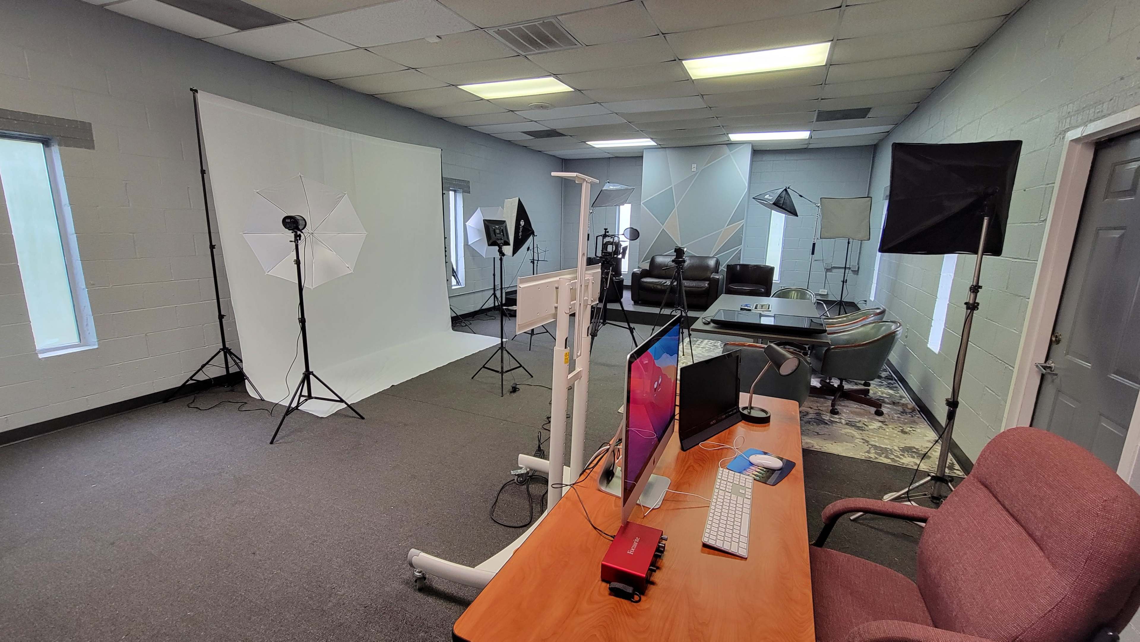 A spacious studio setup with a desk, computer, and various lighting equipment arranged for a photo shoot, alongside a couch and a boat in the background.
