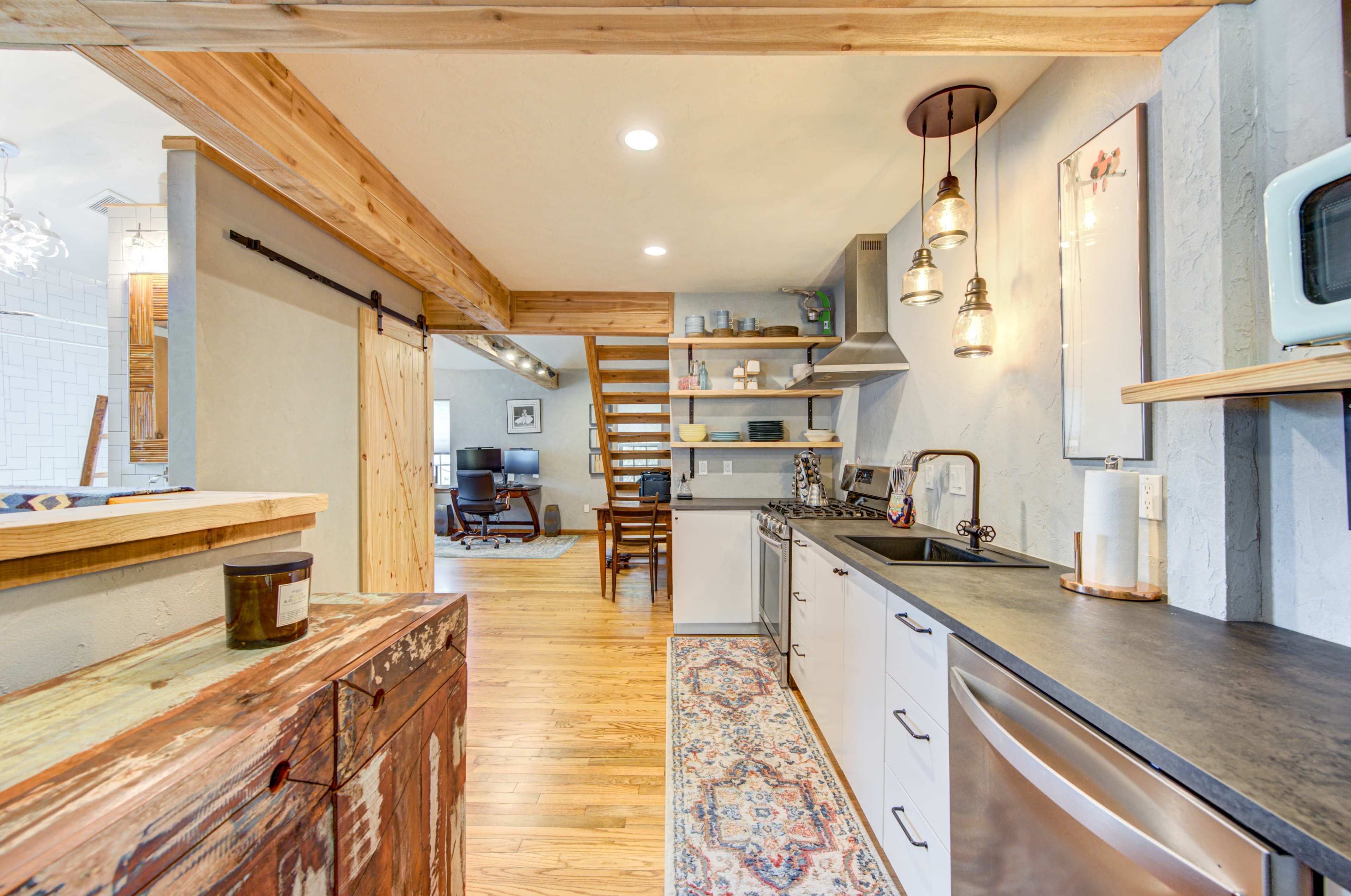 A modern kitchen with wooden beams, pendant lighting, and an open layout leading to a staircase.