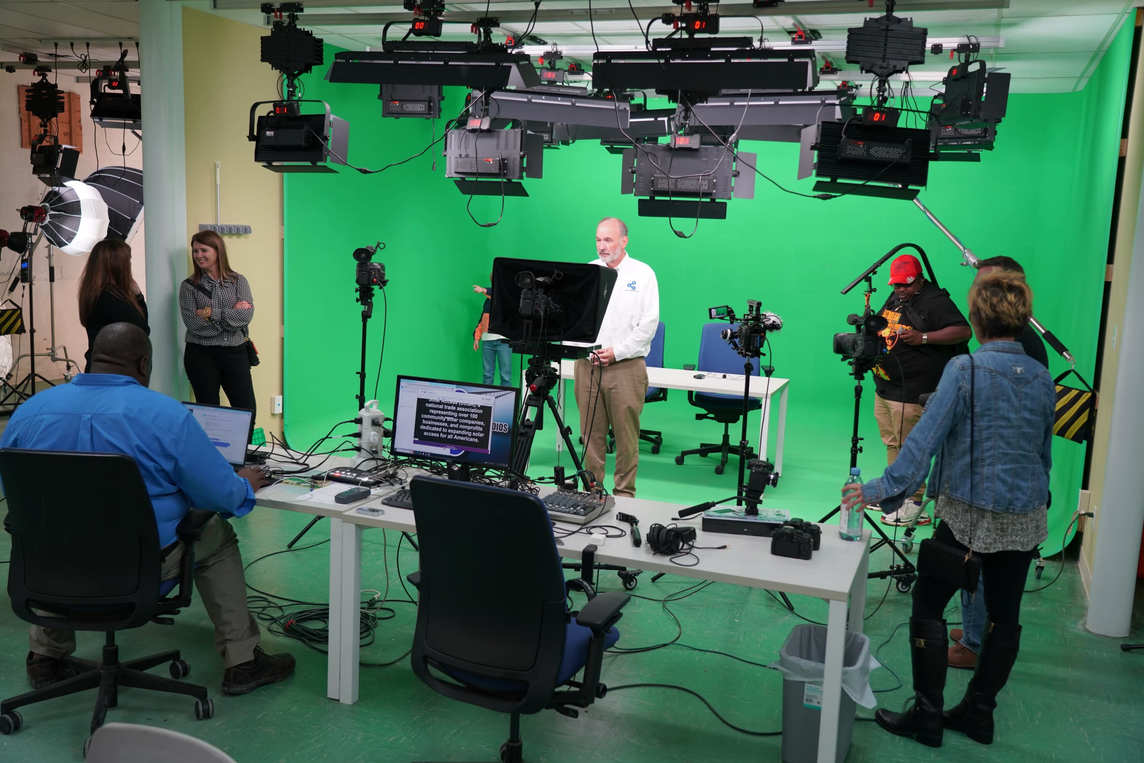 A video production studio with green screen setup, equipped with cameras, lighting, and crew members preparing for filming.