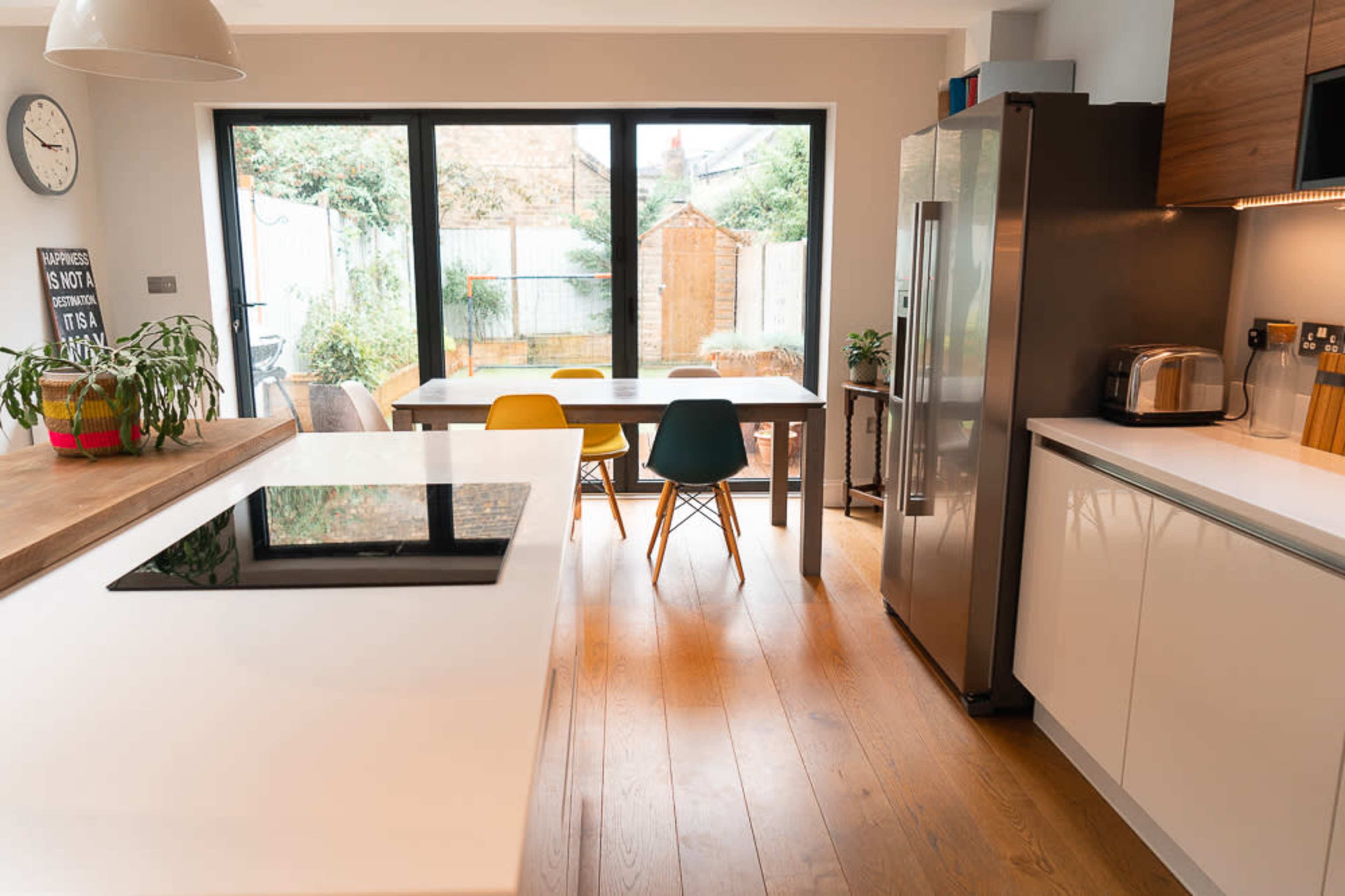A modern kitchen featuring a central island with a cooktop, a dining table with colorful chairs, and large windows providing natural light.