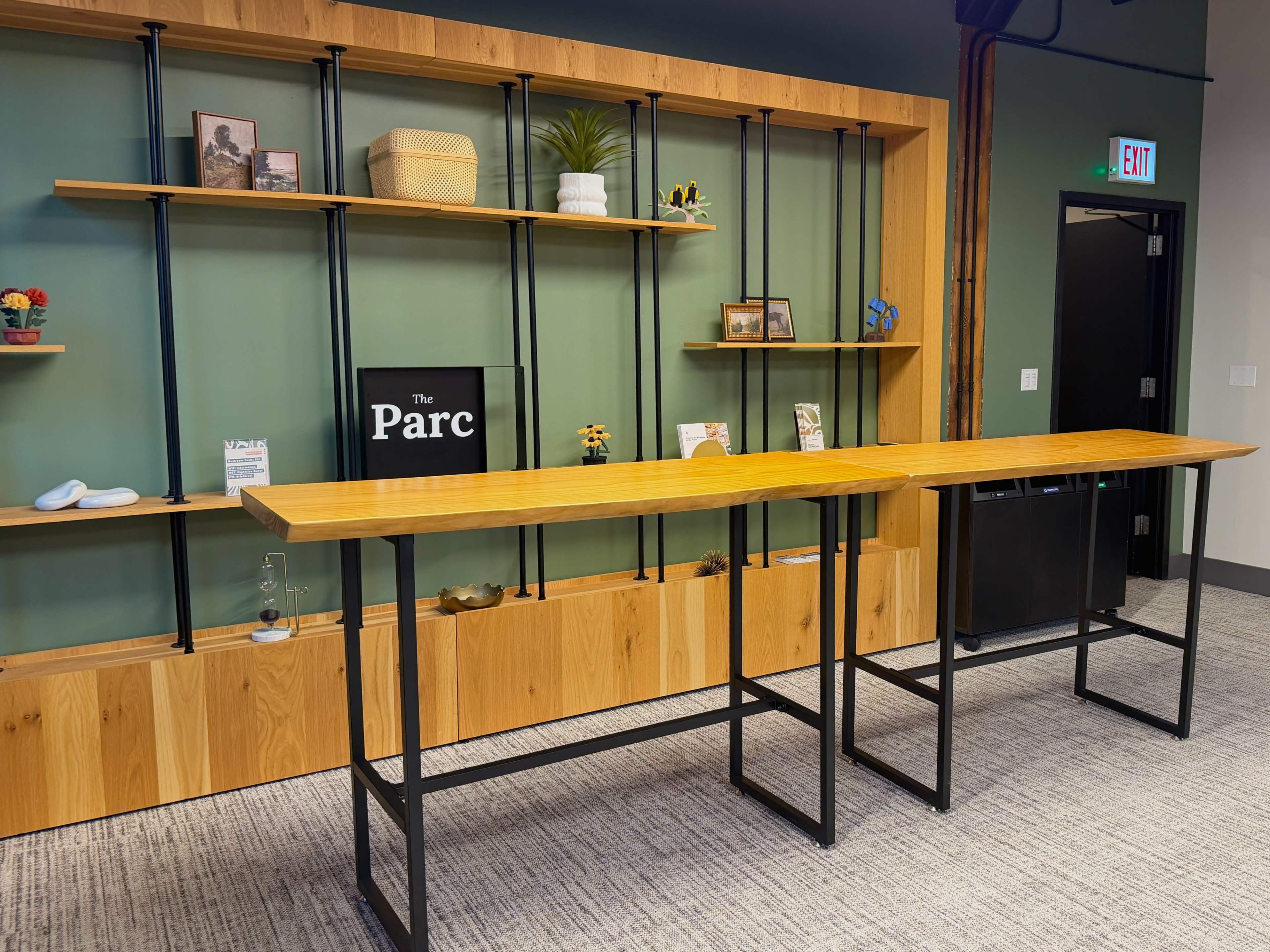 The image shows a modern interior space featuring a long wooden table in front of a stylish shelving unit with decorative items and a sign reading "The Parc."