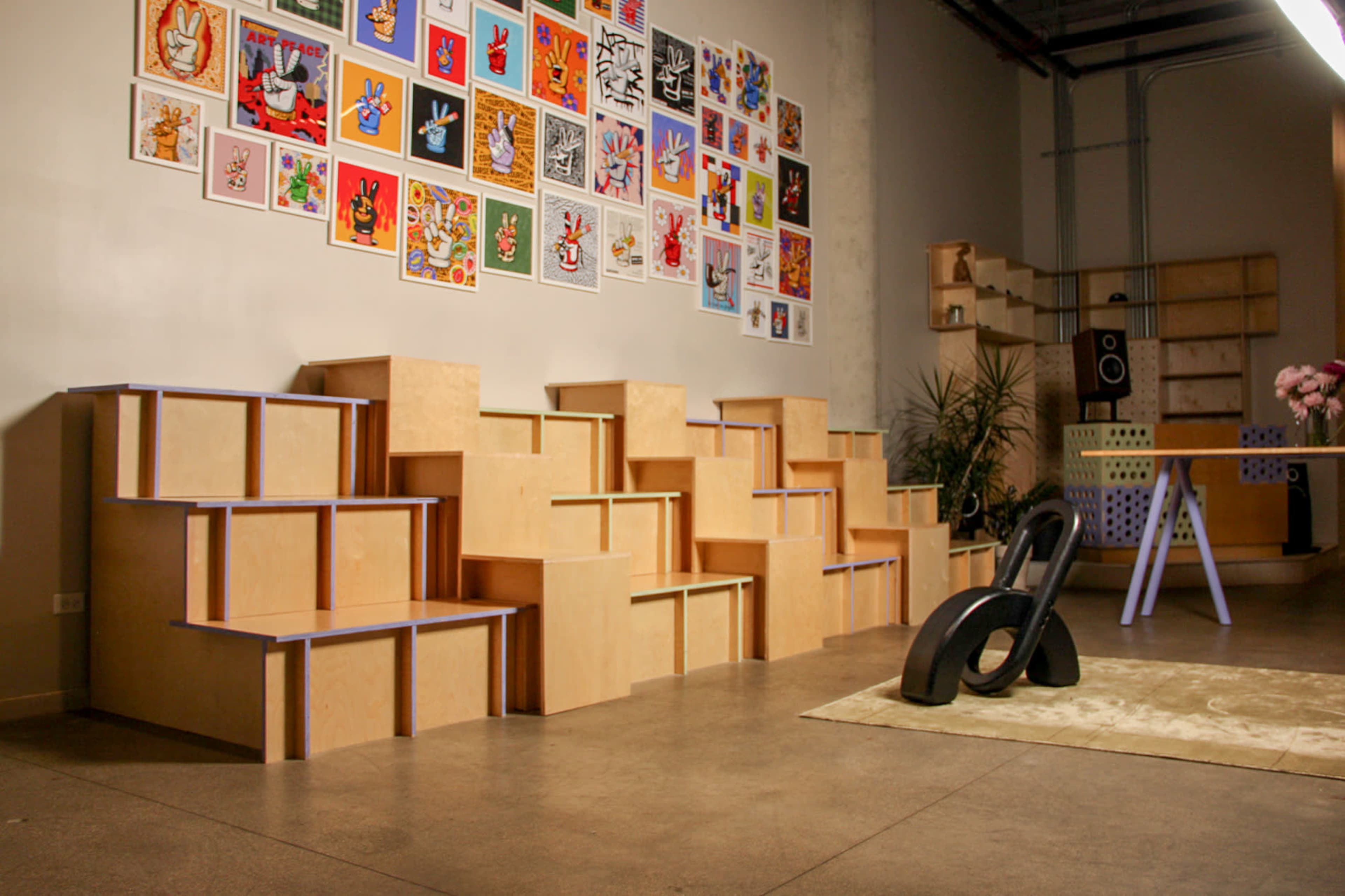 The image shows a modern interior space featuring geometric wooden seating structures against a wall adorned with colorful artwork.