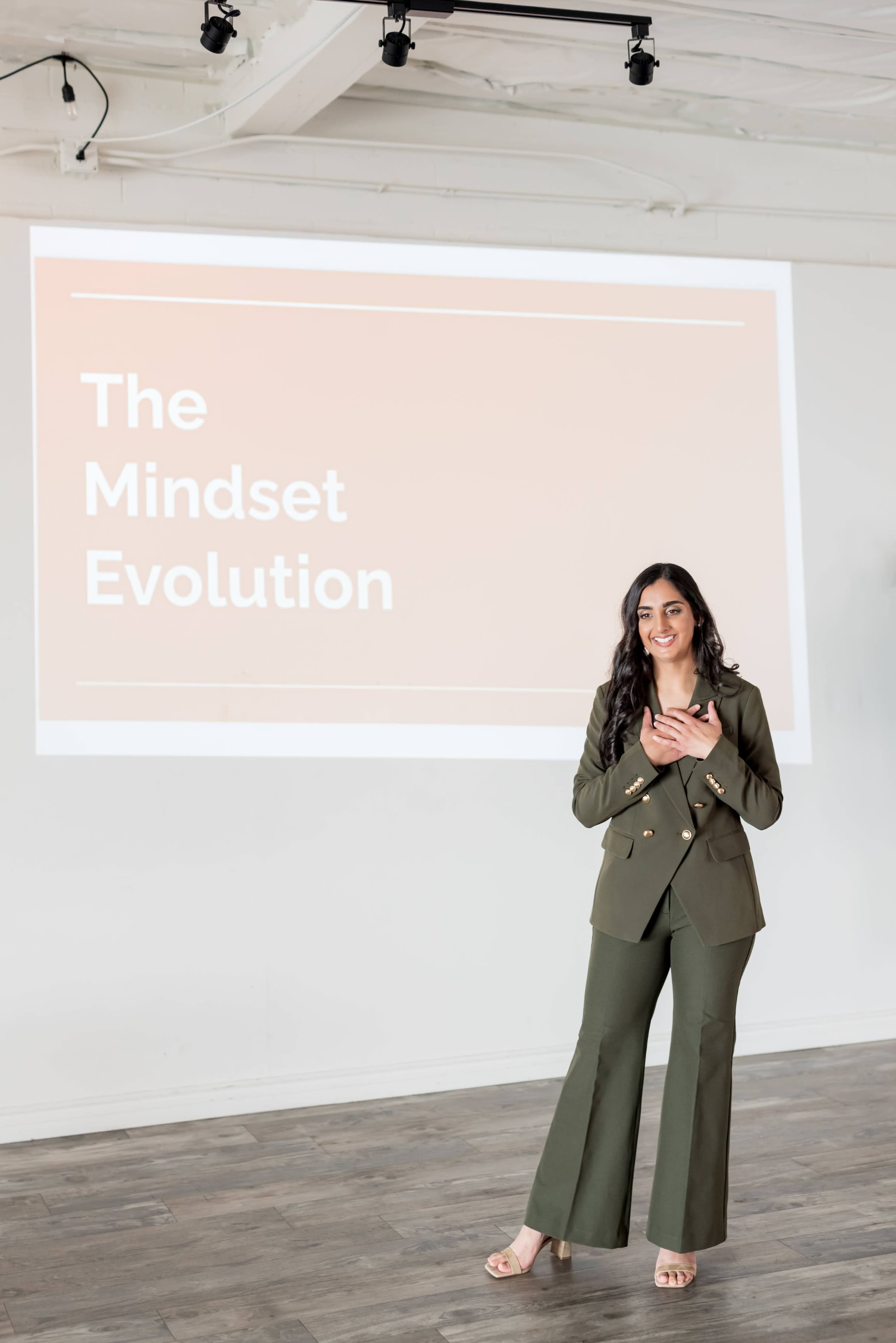 A speaker stands confidently in front of a large presentation screen displaying the title "The Mindset Evolution."