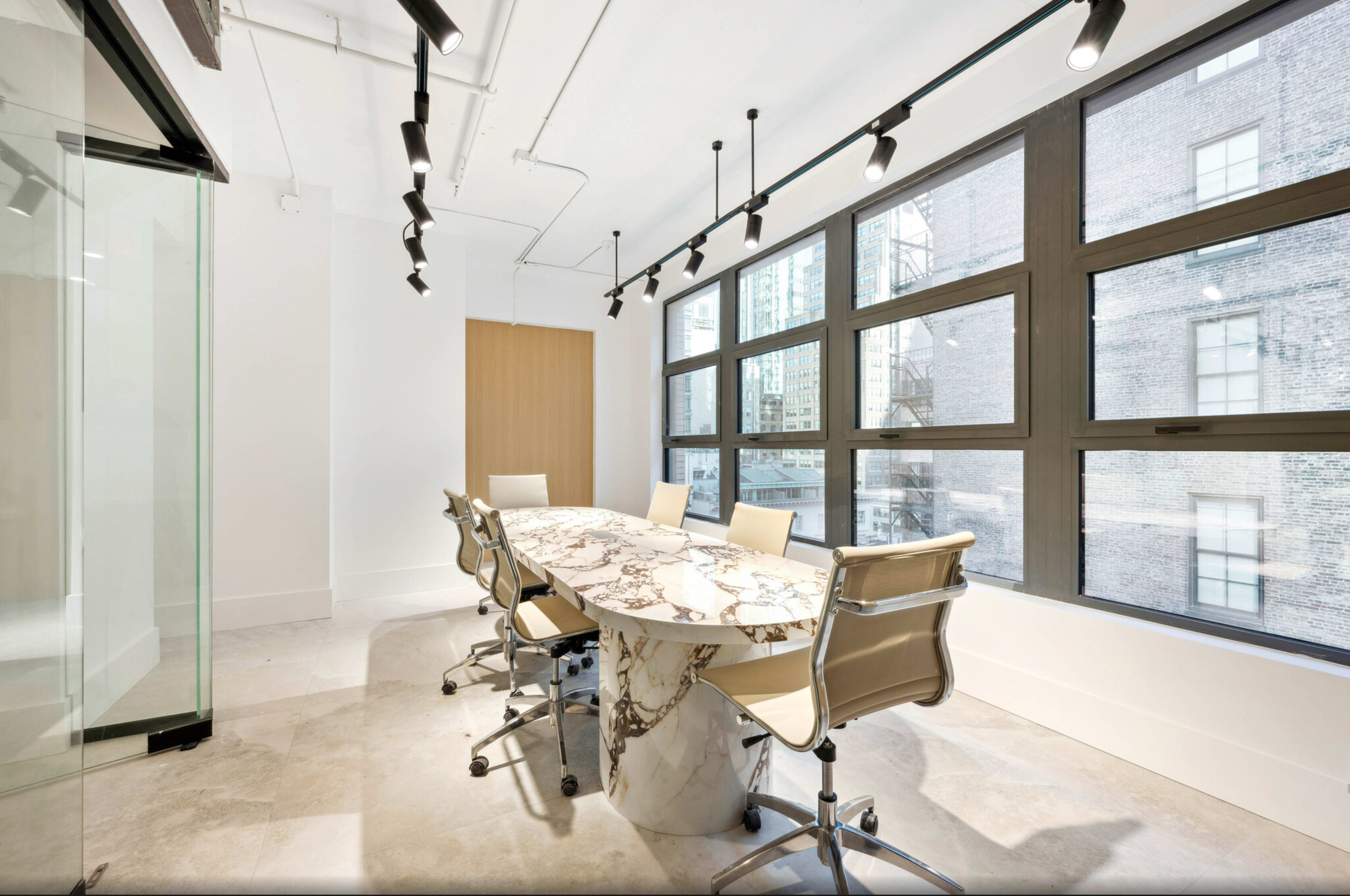 A modern conference room features a marble table surrounded by sleek chairs and large windows allowing natural light to enter.