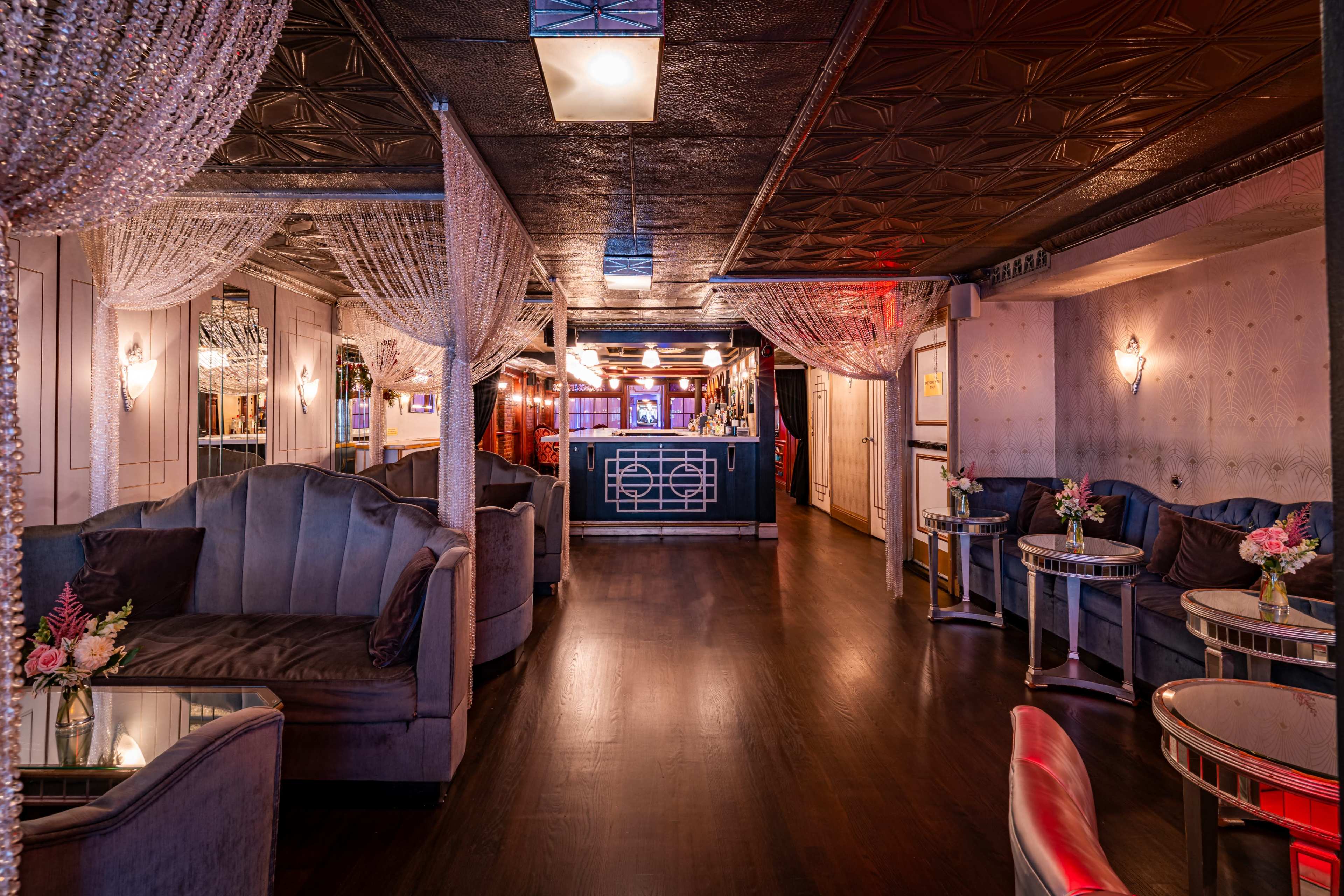 The image shows a dimly lit lounge with plush seating, decorative drapery, and small tables, creating an inviting atmosphere.