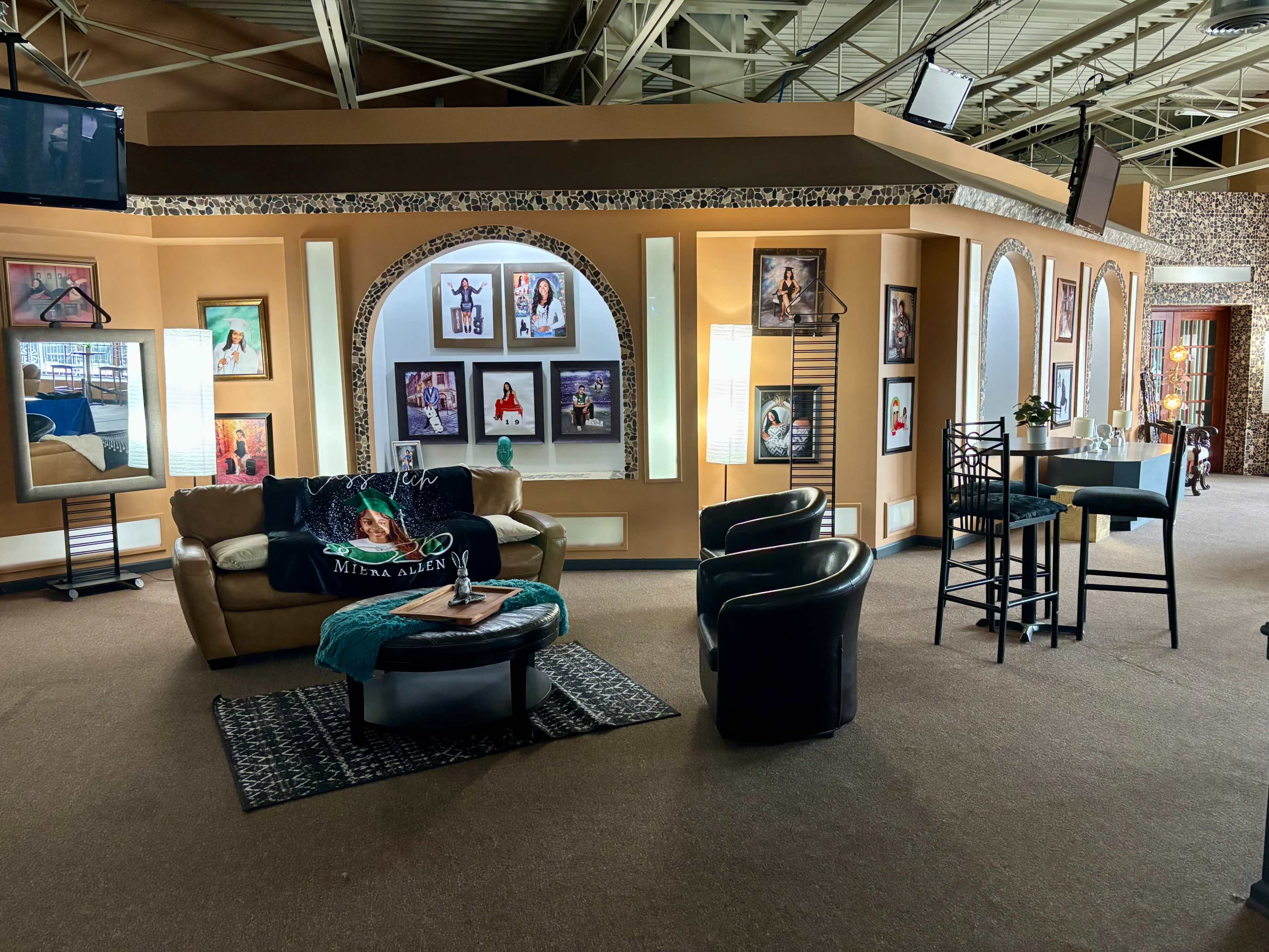 The image shows a spacious interior with a carpeted floor, featuring a sofa, armchairs, and framed artwork on the walls.