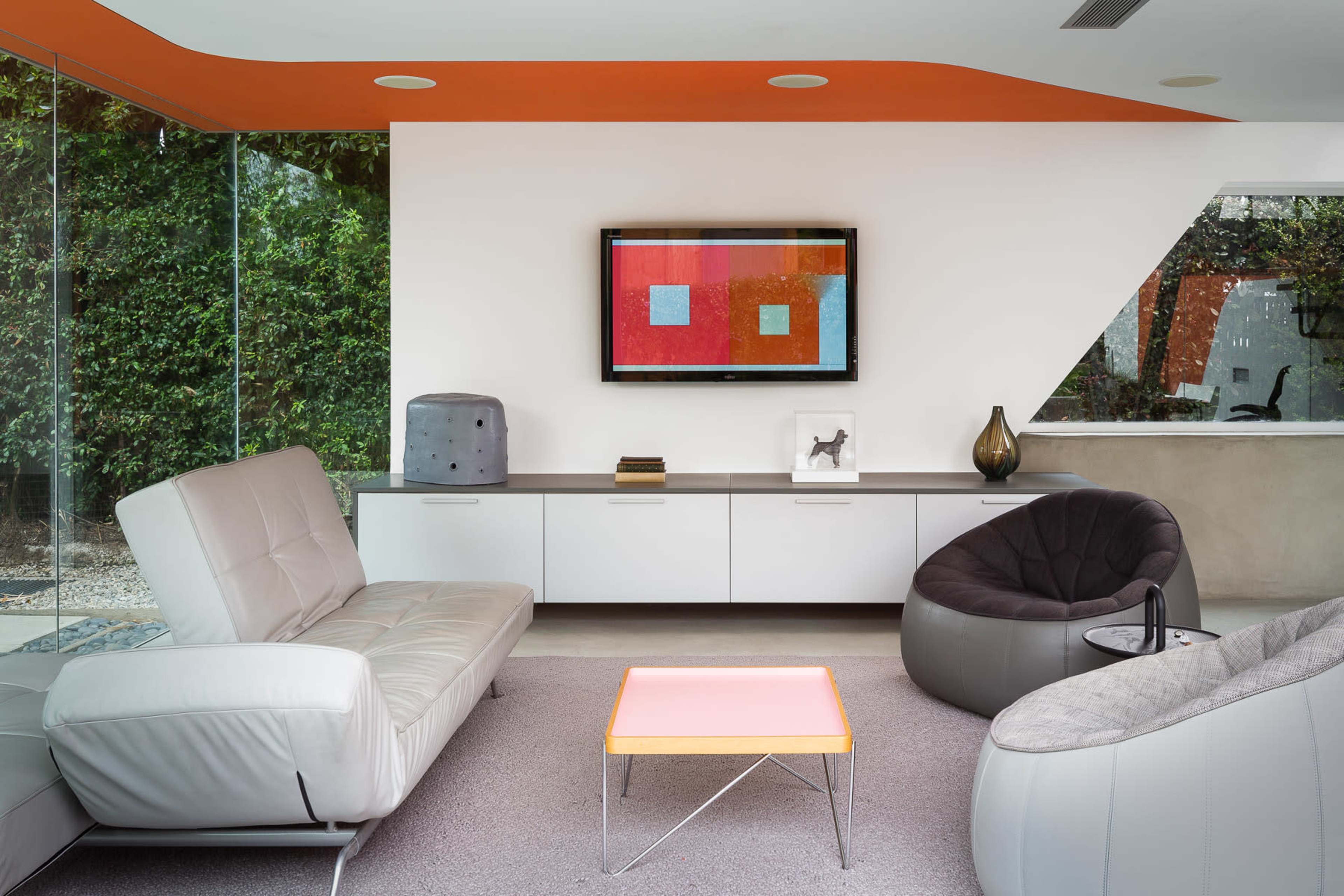A modern living room features a white sofa, a gray armchair, and a pink coffee table, with a television mounted on the wall above a sleek console.