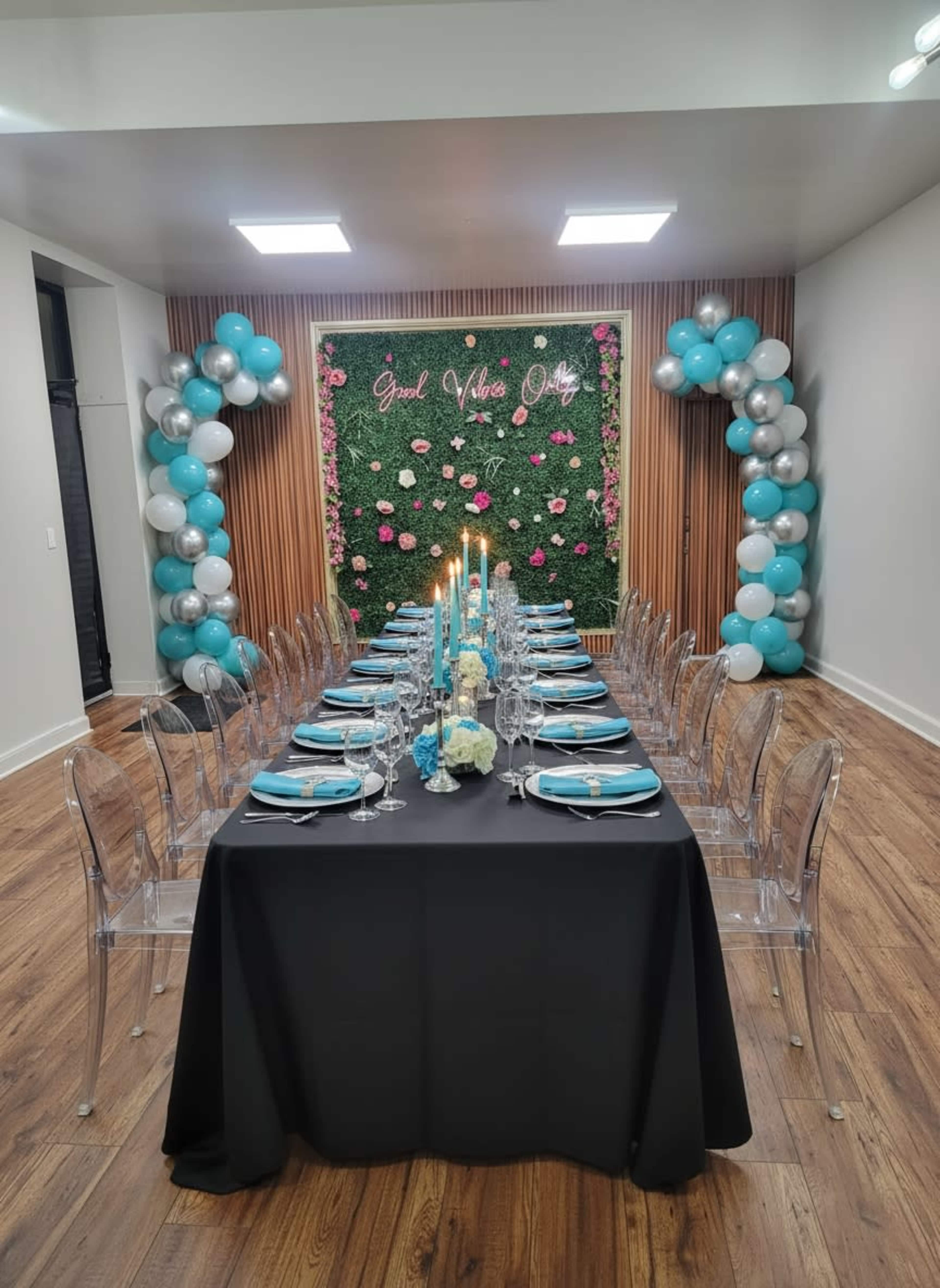 A long dining table is set with blue and white tableware, surrounded by decorated walls featuring green foliage and balloons.