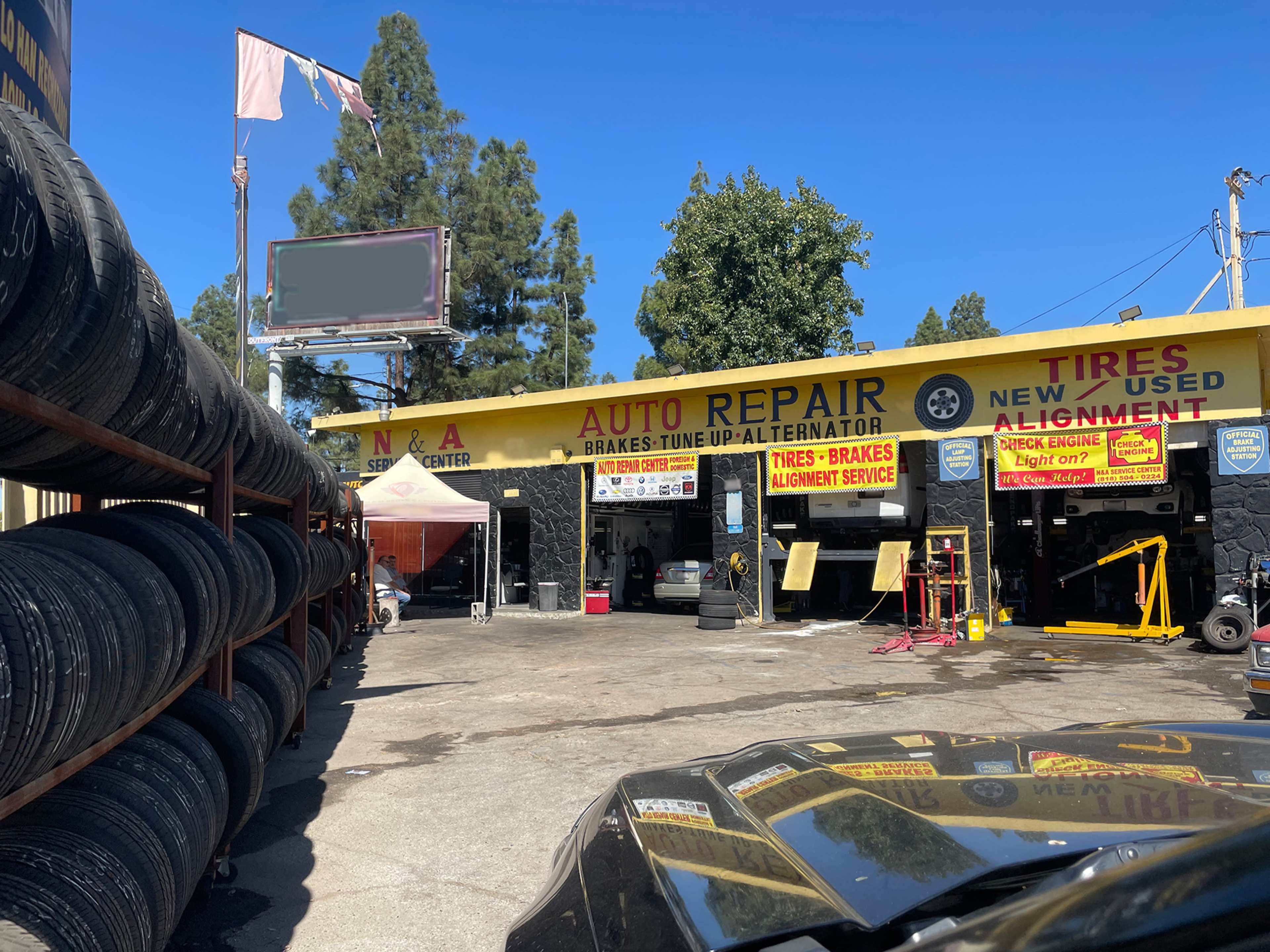 The image shows an auto repair shop with yellow signage advertising services such as brakes, tune-ups, and alignment, alongside stacks of tires displayed outside.