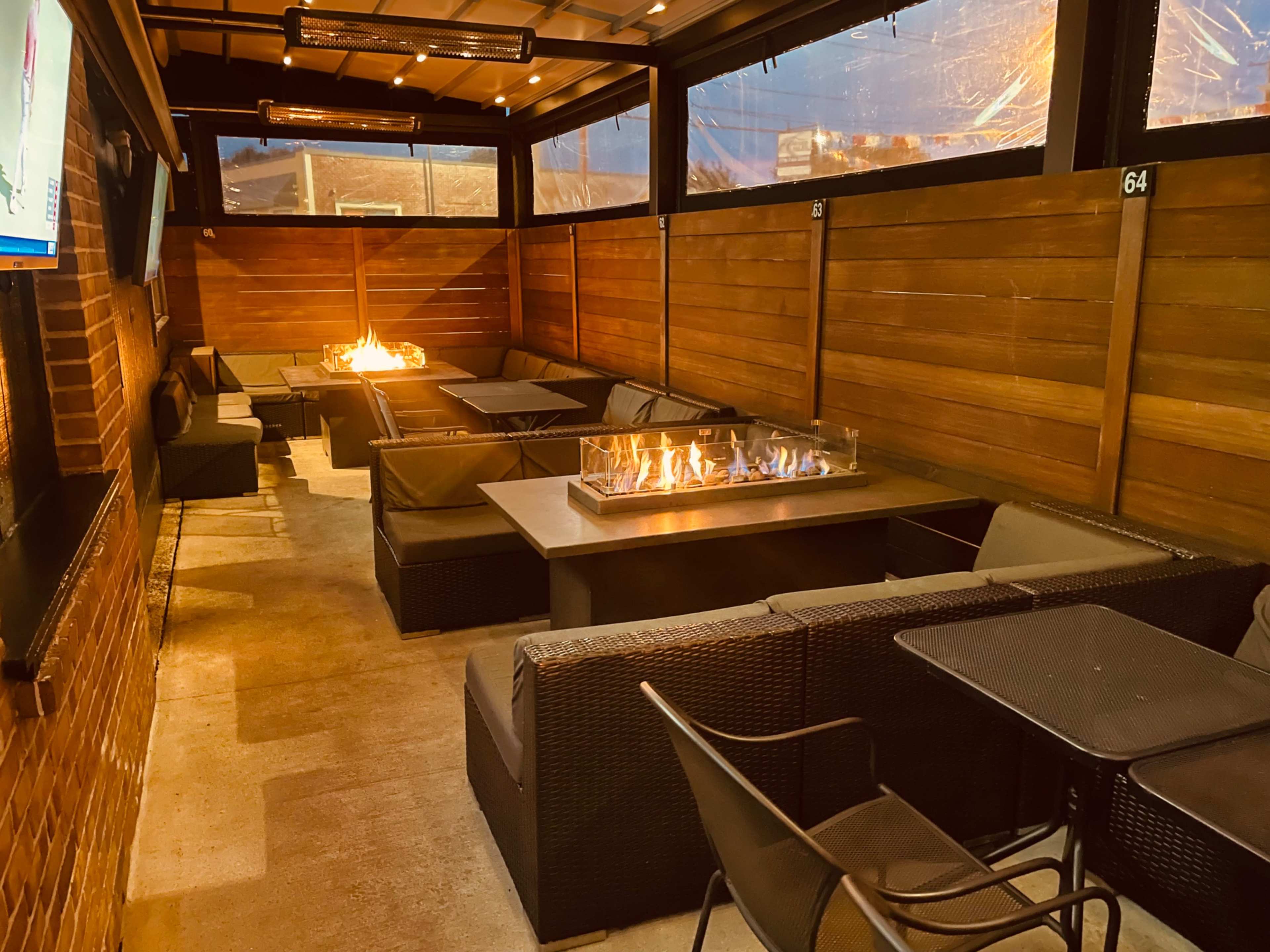 An outdoor seating area with comfortable couches, a fire feature in the center, and protective walls, all covered by a roof.