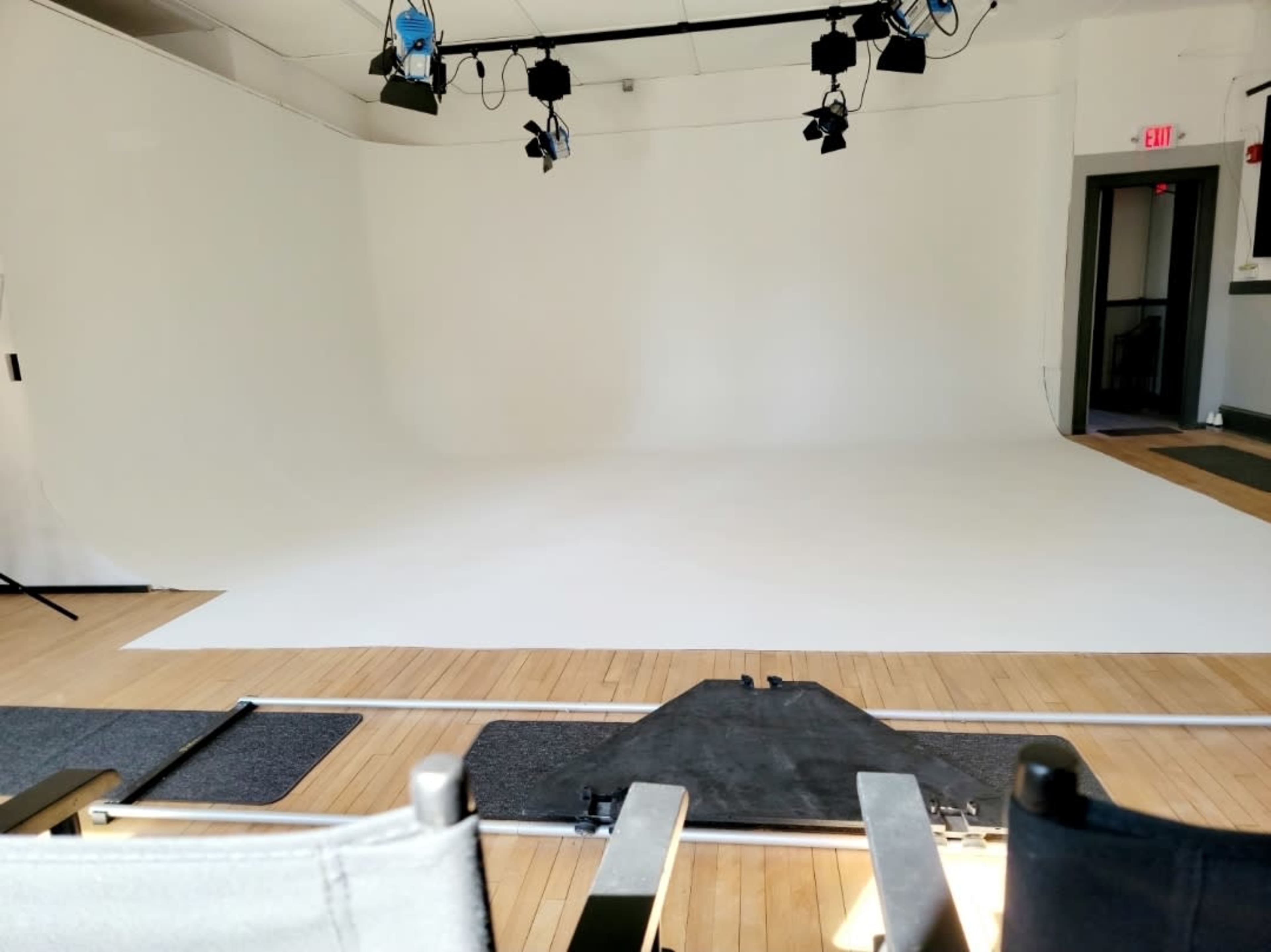 A photography studio with a seamless white backdrop, wooden flooring, and lighting equipment overhead.