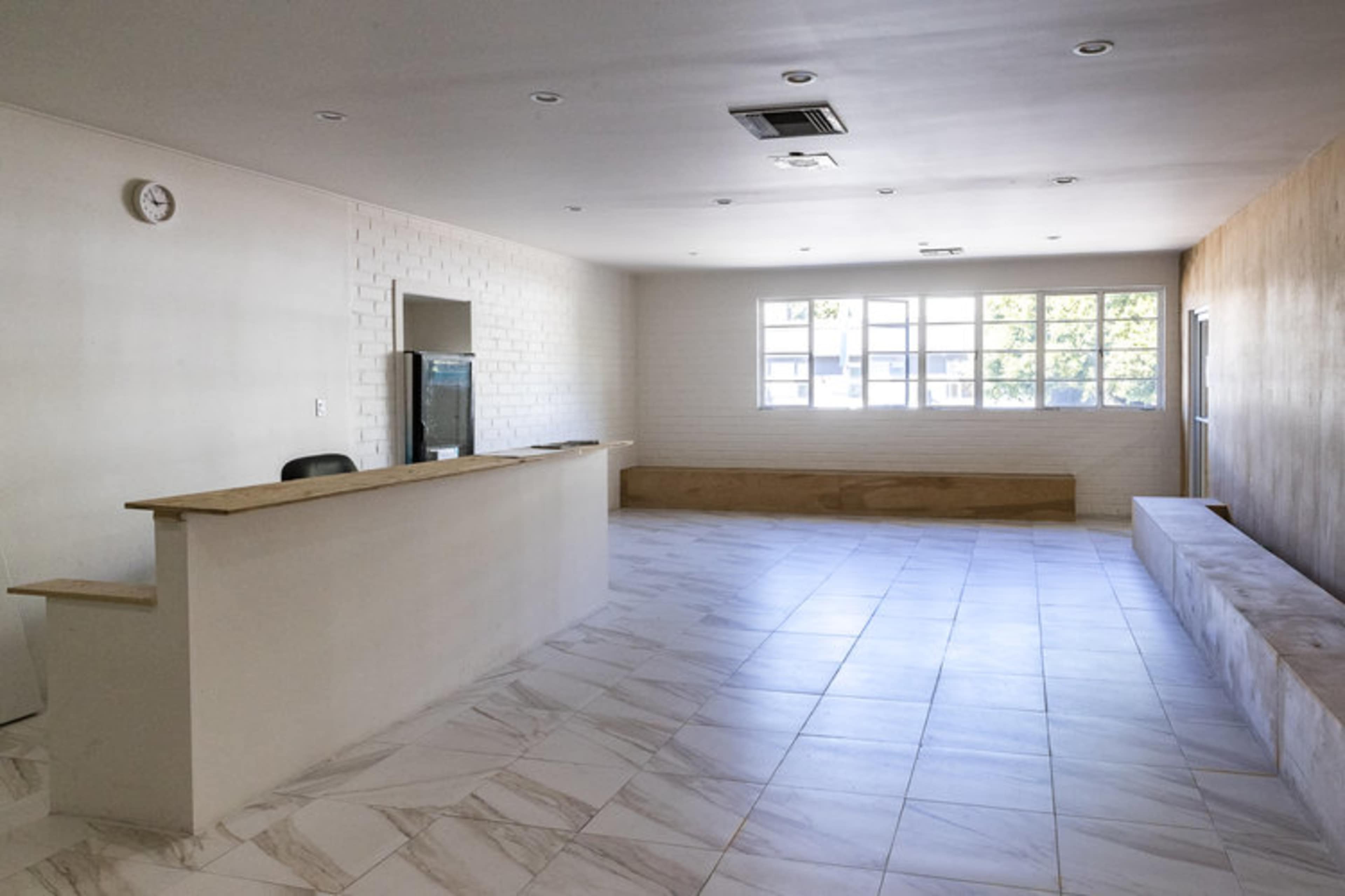 A spacious, empty reception area with a white counter and large windows letting in natural light.