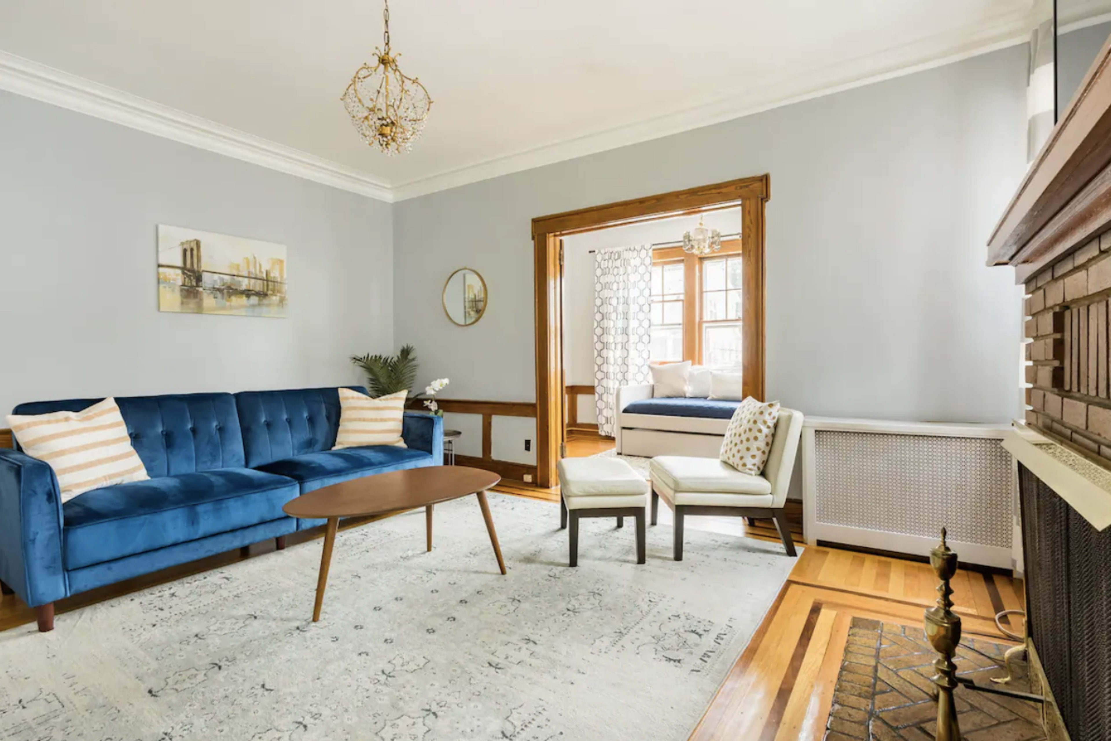 A living room with a blue velvet couch, a wooden coffee table, and a view of a connected bedroom through an archway.