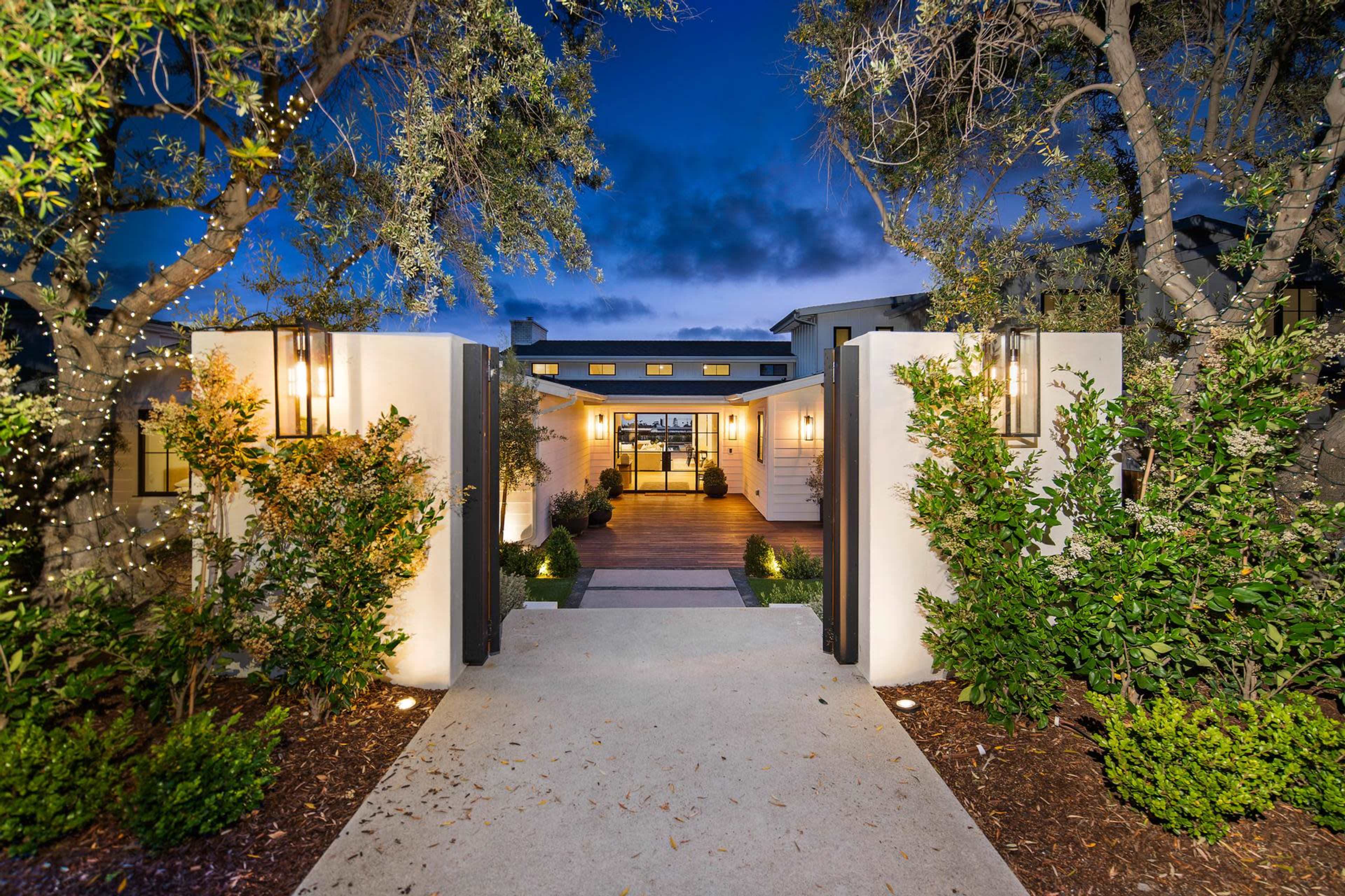A modern home is visible through a well-lit entrance flanked by trees, with a pathway leading to an inviting front door.